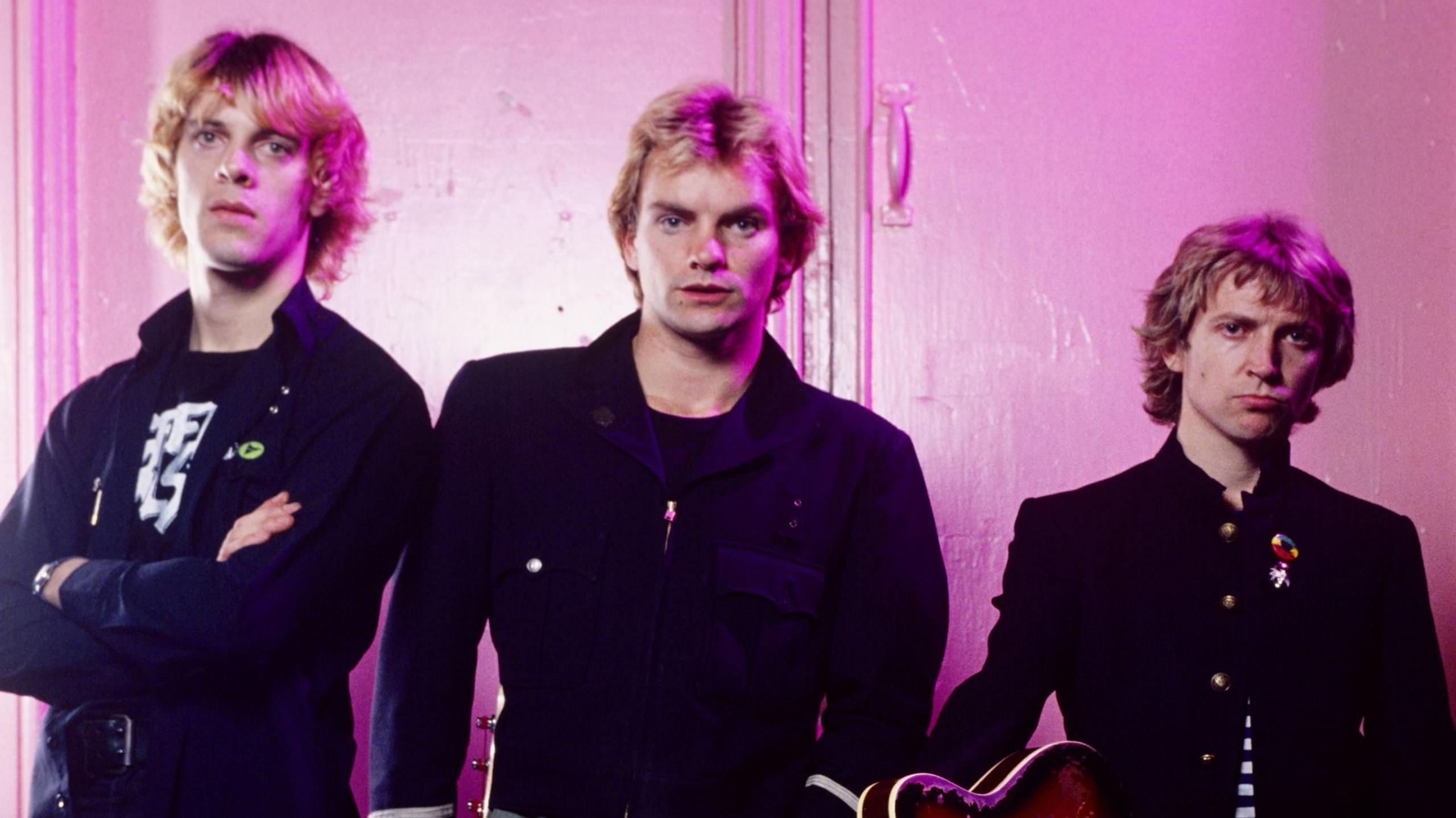 The Police pose against a plain wall, with pink lighting, during a portrait session in 1979