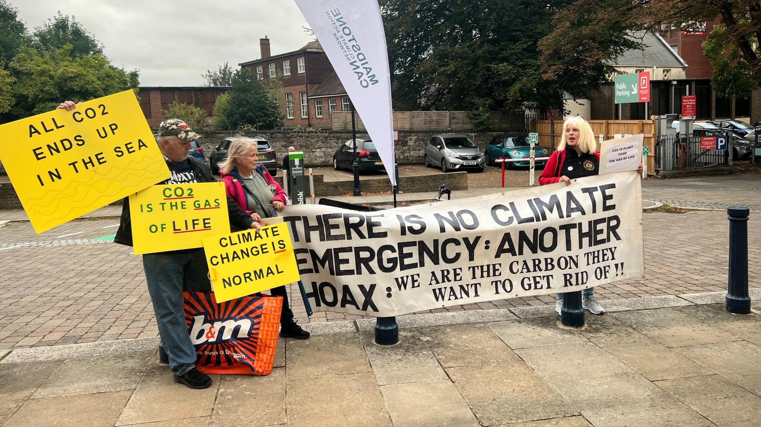 Two women and one man stand outside County Hall in Maidstone holding a series of banners. They say "There is no climate emergency: Another hoax: We are the carbon they want to get rid of!!", "Climate change is normal", "CO2 is the gas of life", and "All CO2 ends up in the sea".