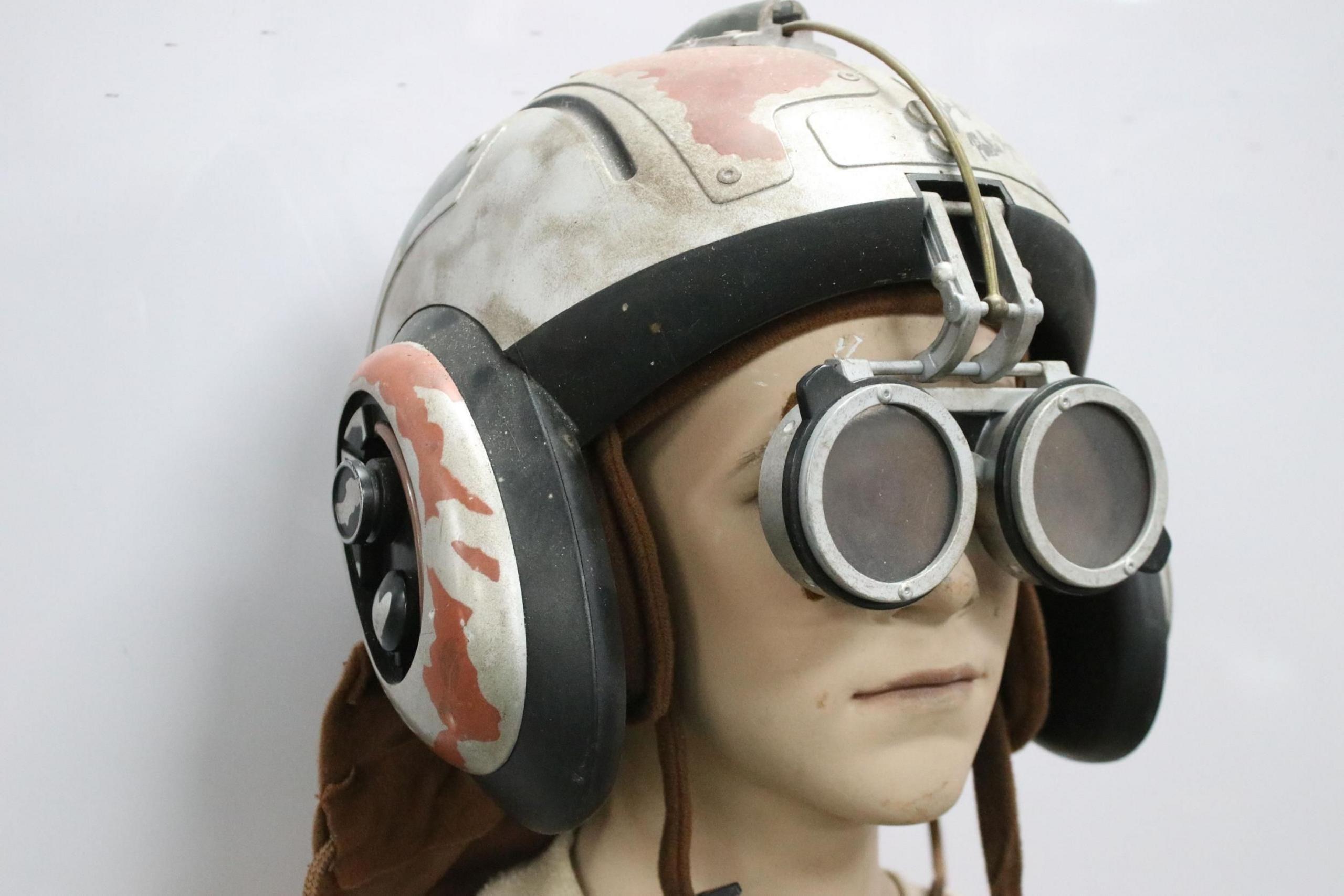 A replica of a small child wearing a white helmet with goggles which swing down from the top of the helmet.