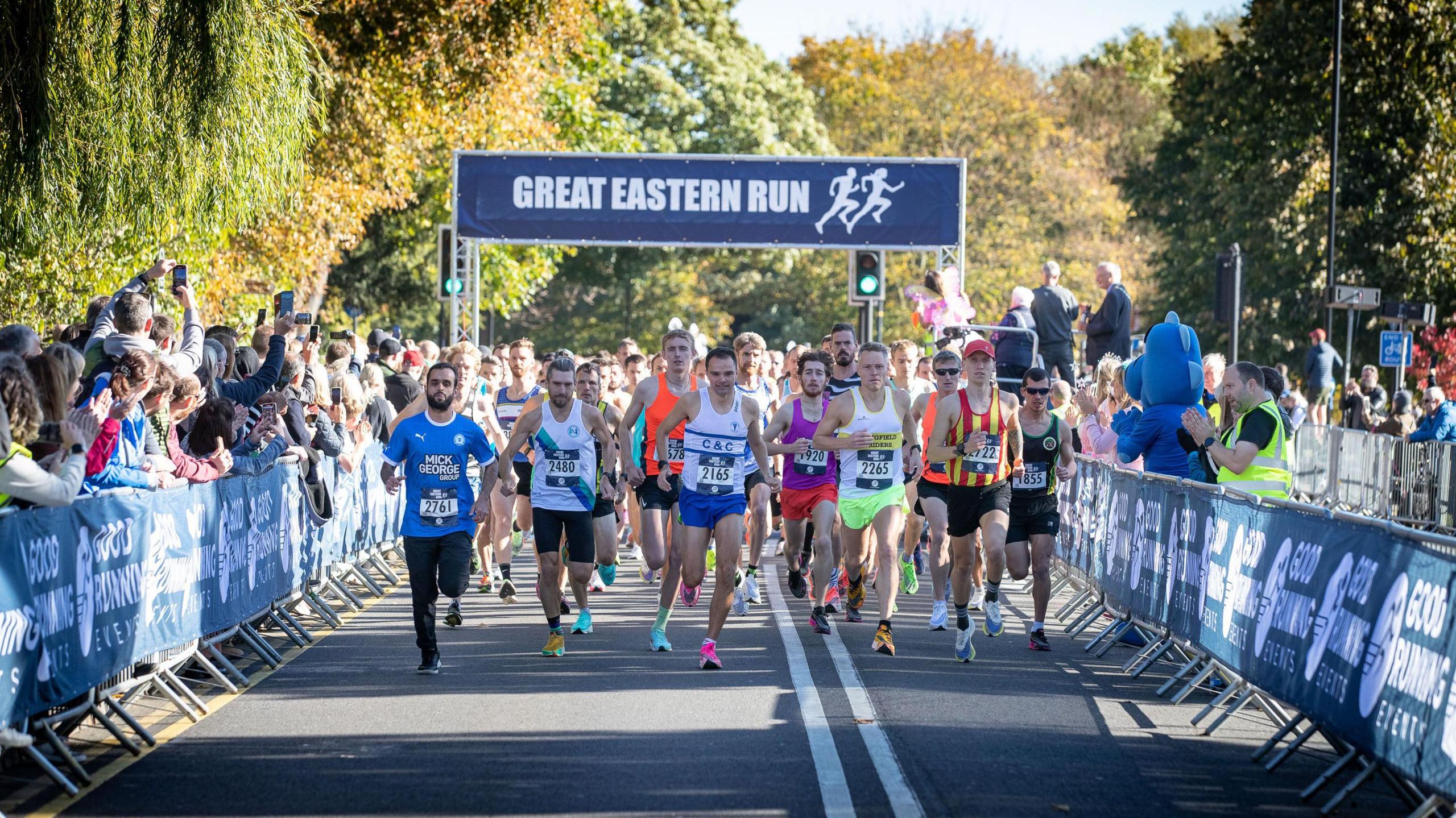 Runners running just after the start line- with a Great Eastern Run banner in the background and members of the public standing on either side of the track, clapping their hands.