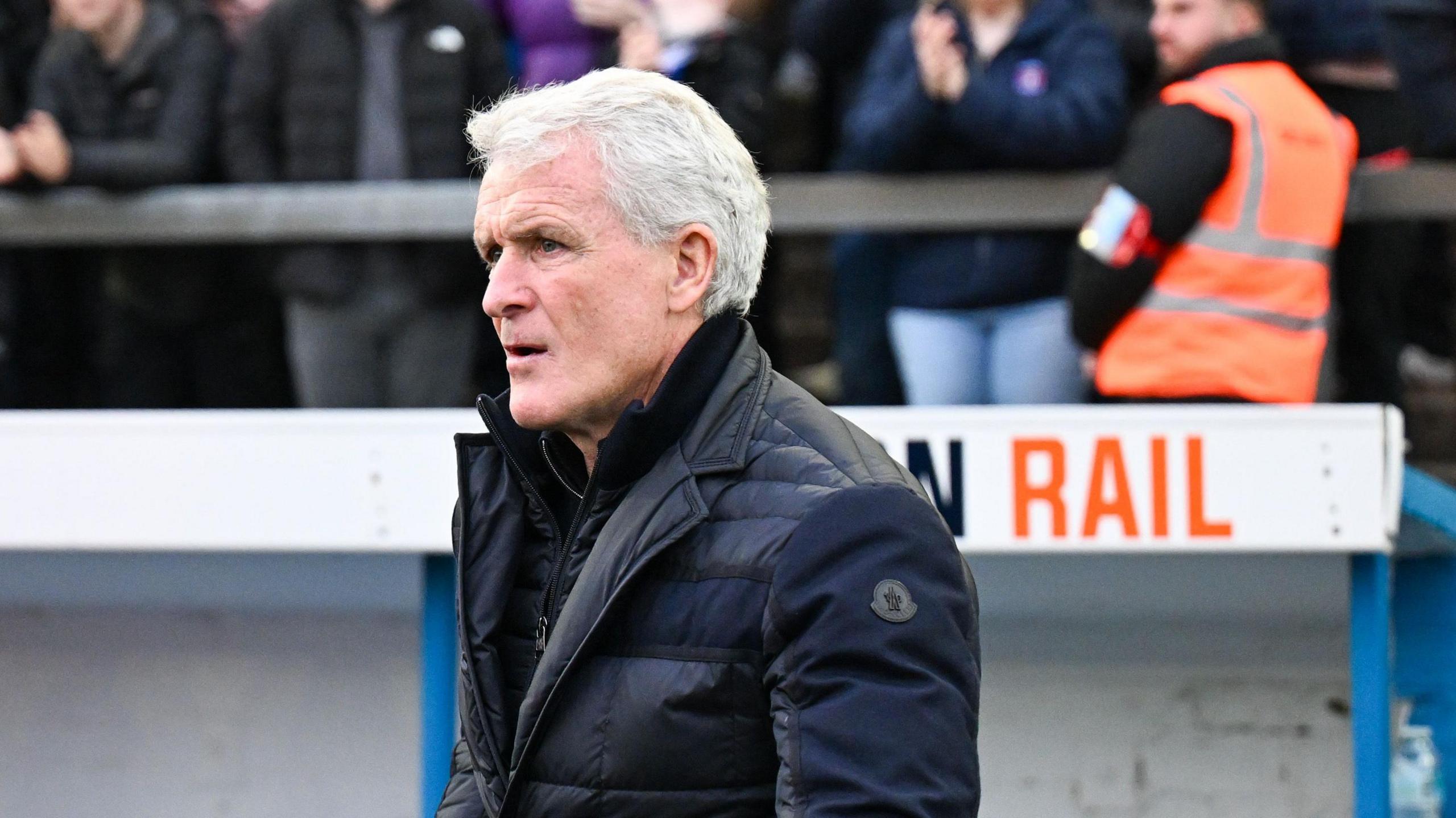 Mark Hughes standing in front of the dugout at Brunton Park