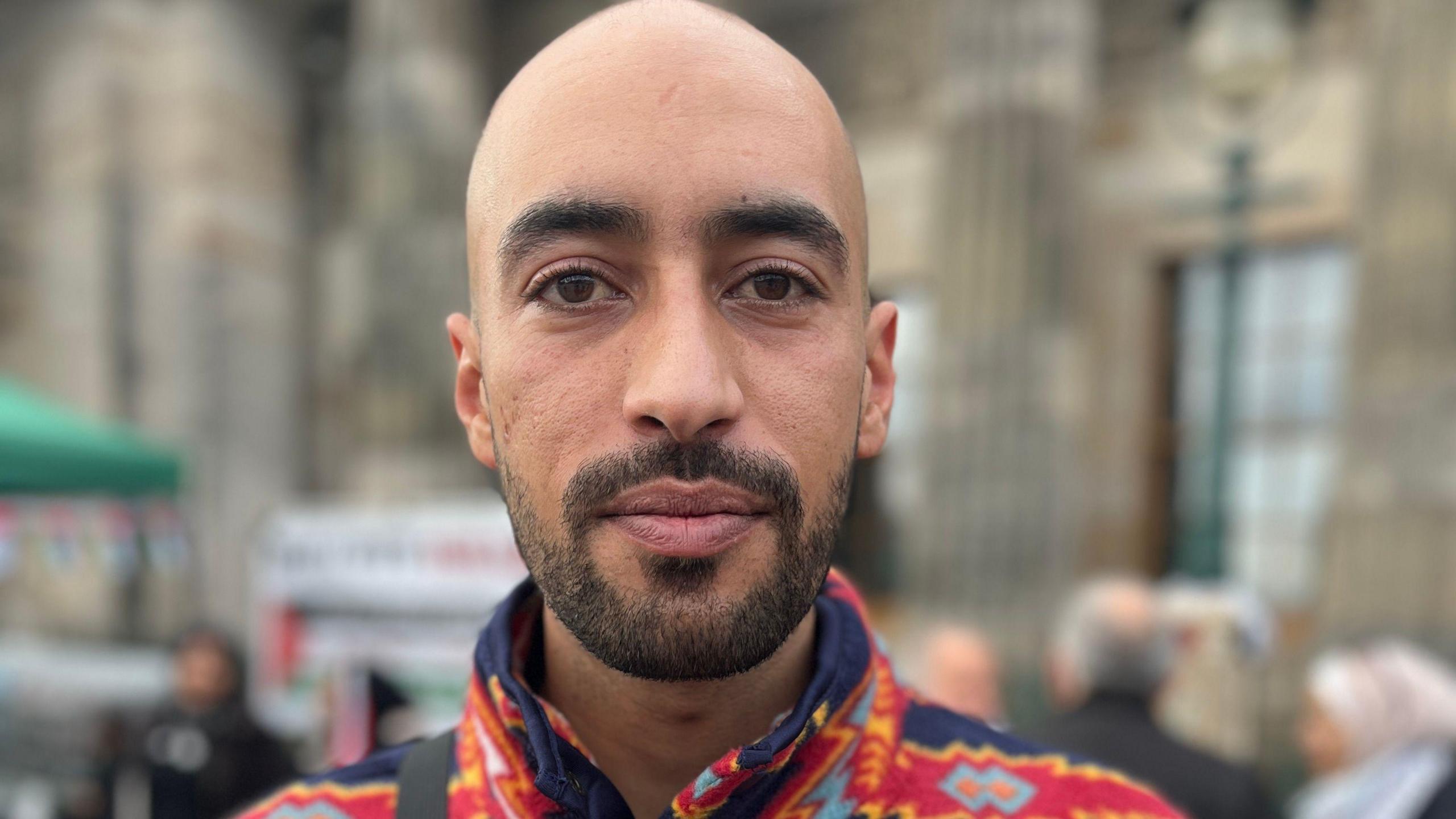 Majdi Awwad, a Palestinian man. He has a bald head, a dark moustache and beard. He is wearing a patterned top.