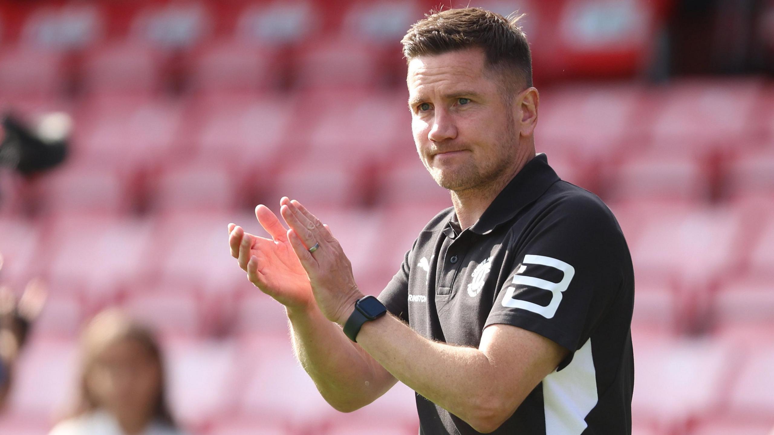 Crewe manager Lee Bell claps the fans in his black and white club polo shirt at the end of the 3-1 win at Salford
