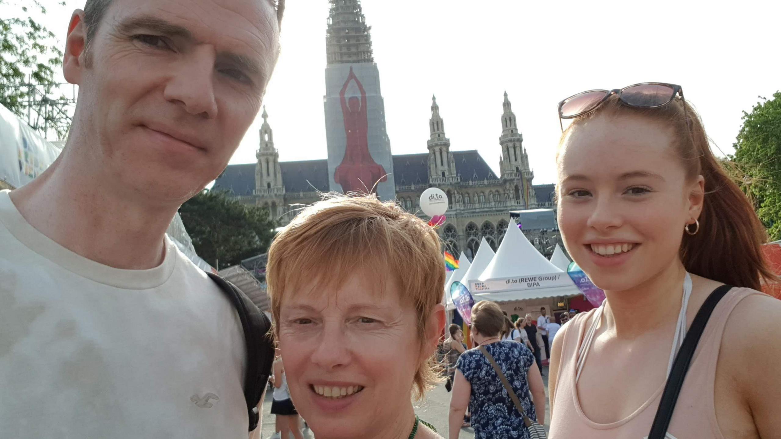 A man, woman and teenage girl take a selfie in a crowded marketplace