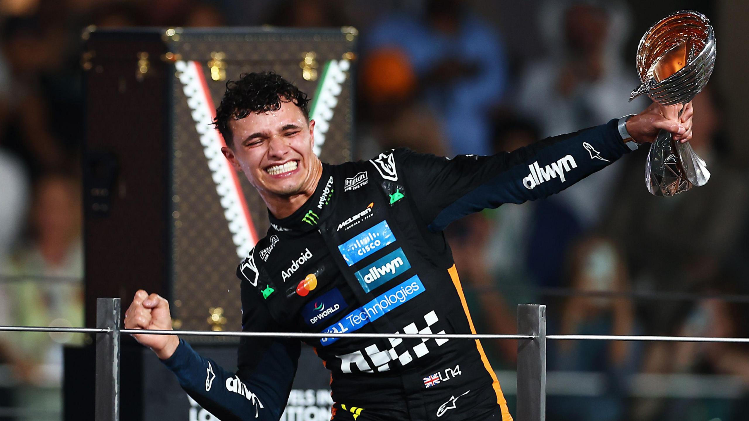 Formula One driver Lando Norris holds a trophy in his hand and smiles whilst celebrating his win