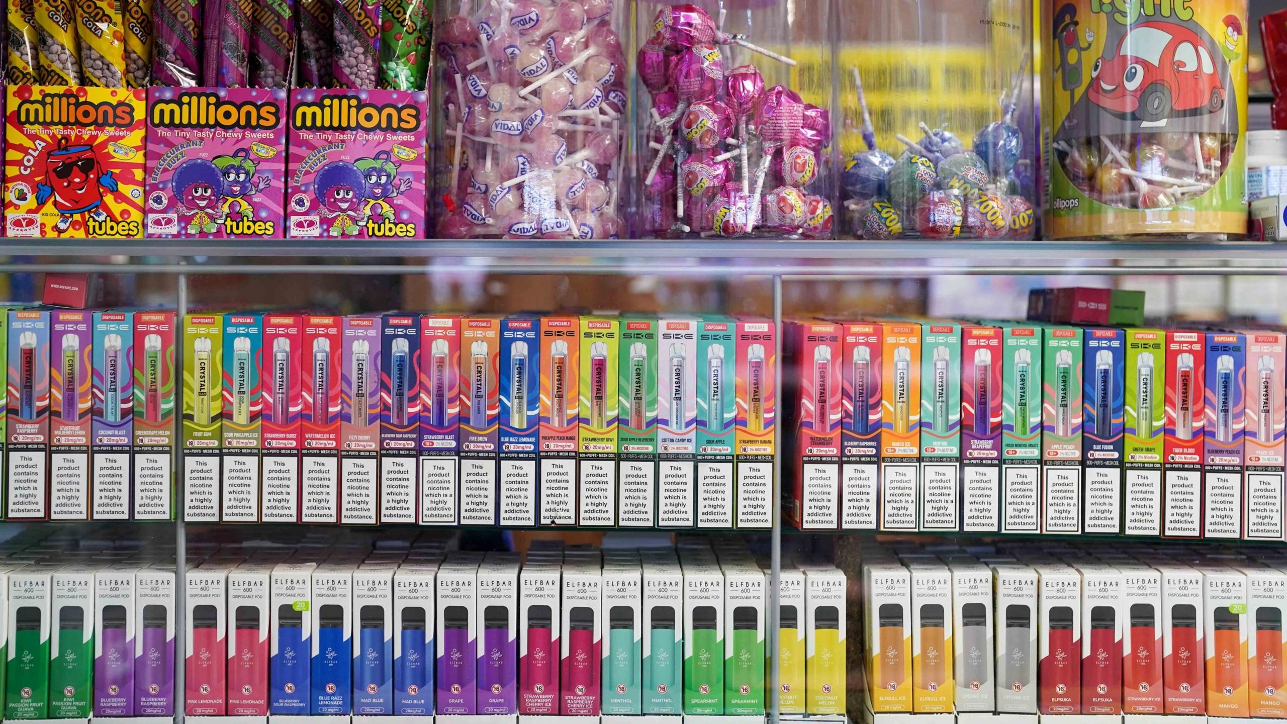 Disposable vapes on display on shop shelves below jars of sweets