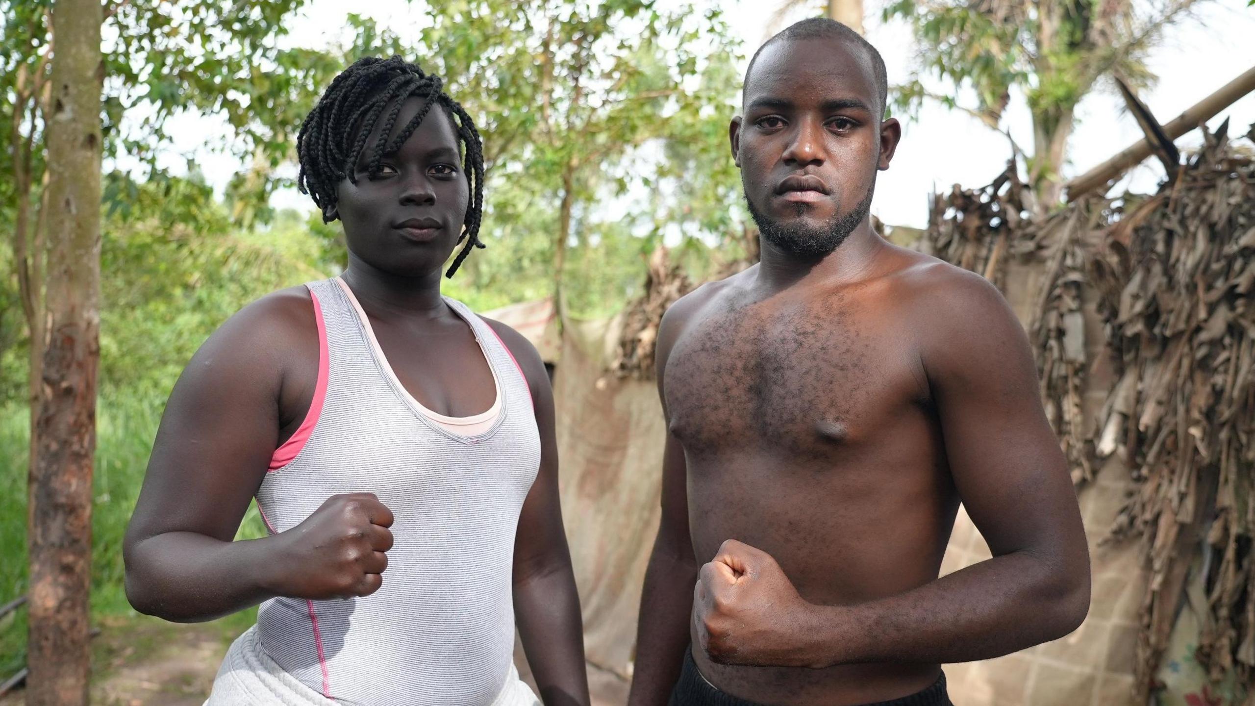 Lamono Evelyn wears a white singlet and Jordan Loverine poses shirtless as both hold up a clenched fist towards the camera