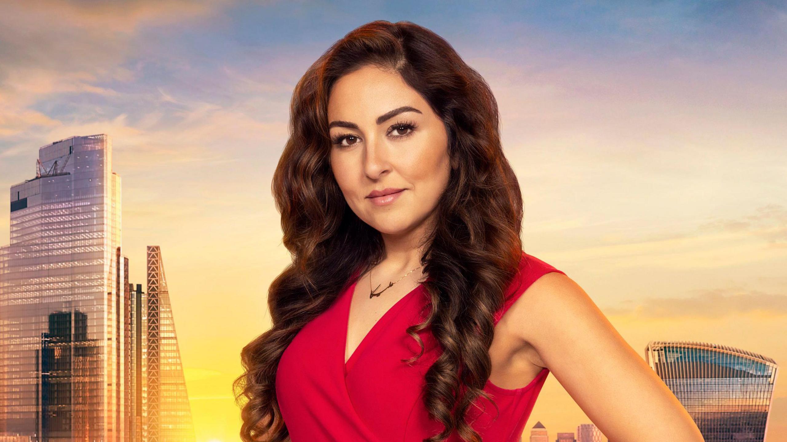 The official Apprentice portrait photo of candidate Melica Morshiri. She wears a red dress while standing in front of a sunlit London skyline.