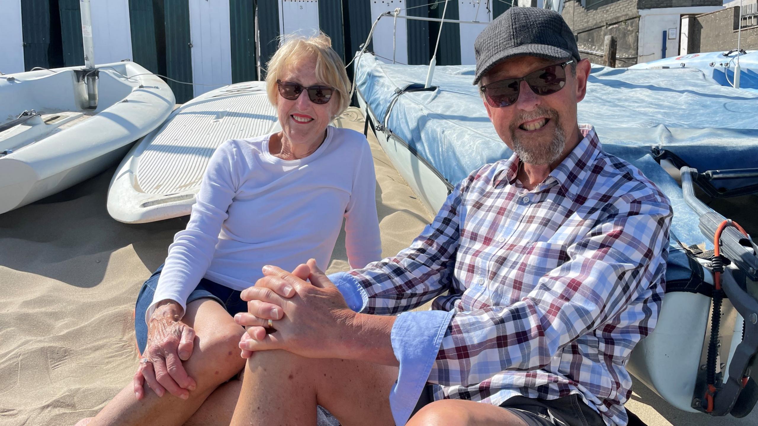 Heather and Alan Jenkins sat down on sand at Porth Mawr beach, Abersoch, in shorts and wearing sunglasses