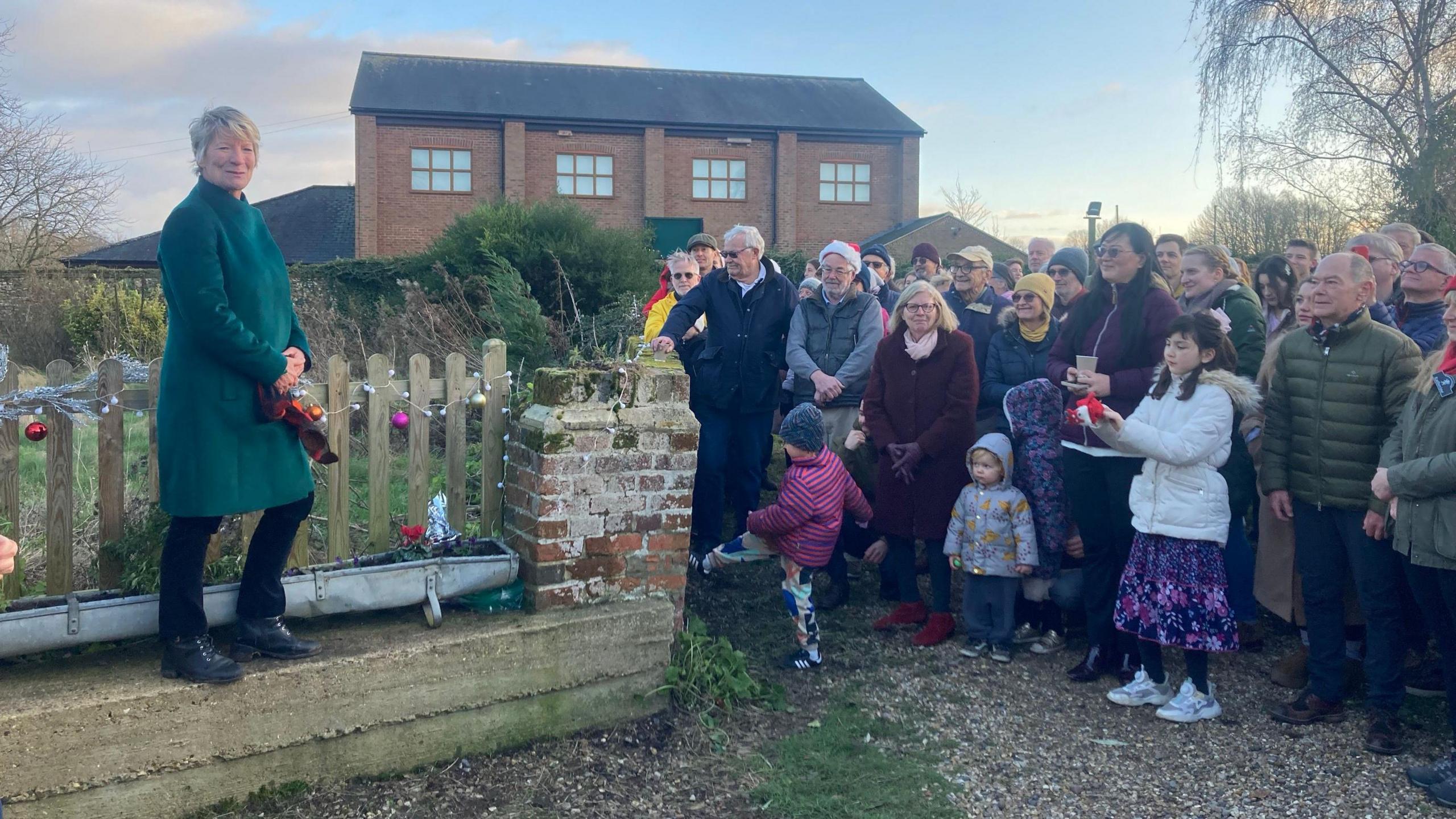 Pippa Heylings is standing on a wall to the left of the photo. On the right hand side there are at least 20 people looking in her direction, wearing coats, scarfs and hats.