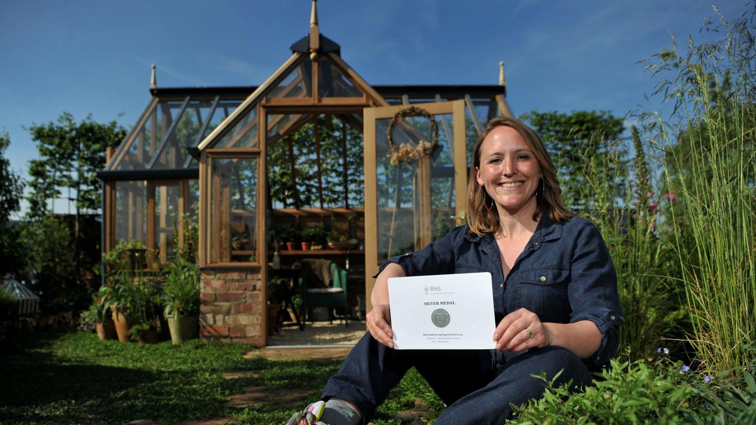 Laura Ashton-Phillips holding her silver medal certificate in her garden