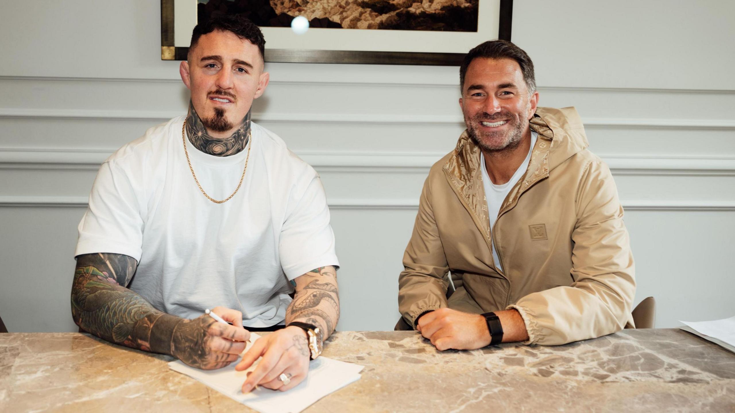 Tom Aspinall signs a contract beside Eddie Hearn