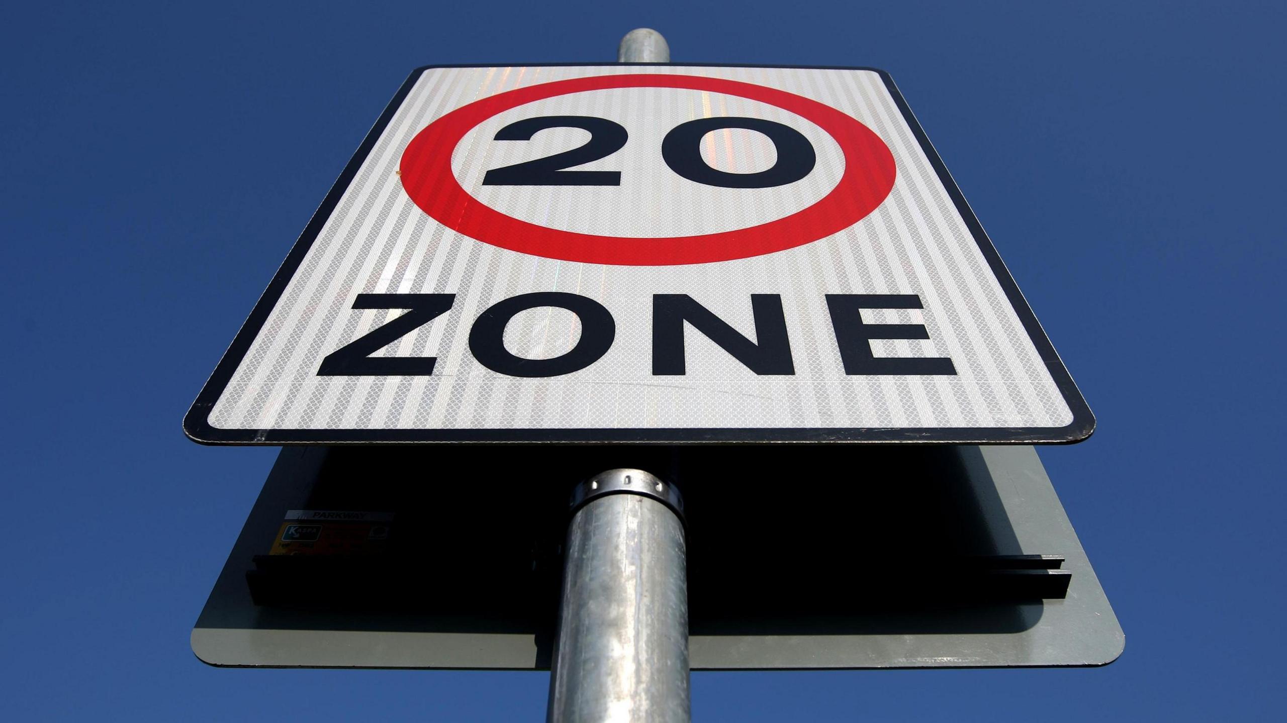 A photo of a 20mph zone sign, taken from below, with a clear blue sky behind it.