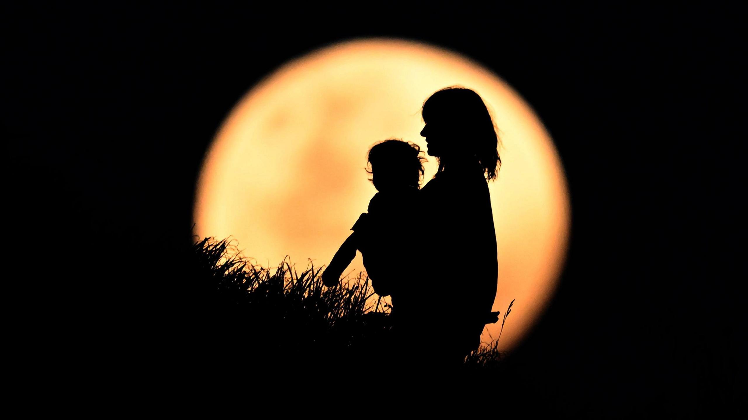 woman and child silhouettes against a blood moon