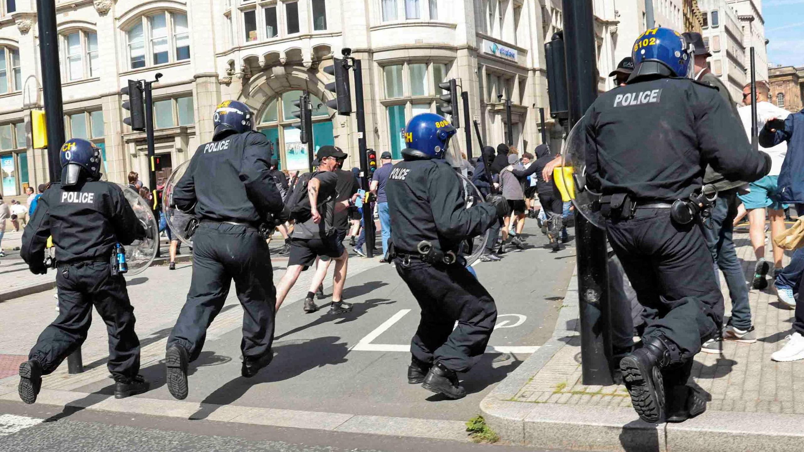 Police officers in riot gear charge at protesters near the Pier Head