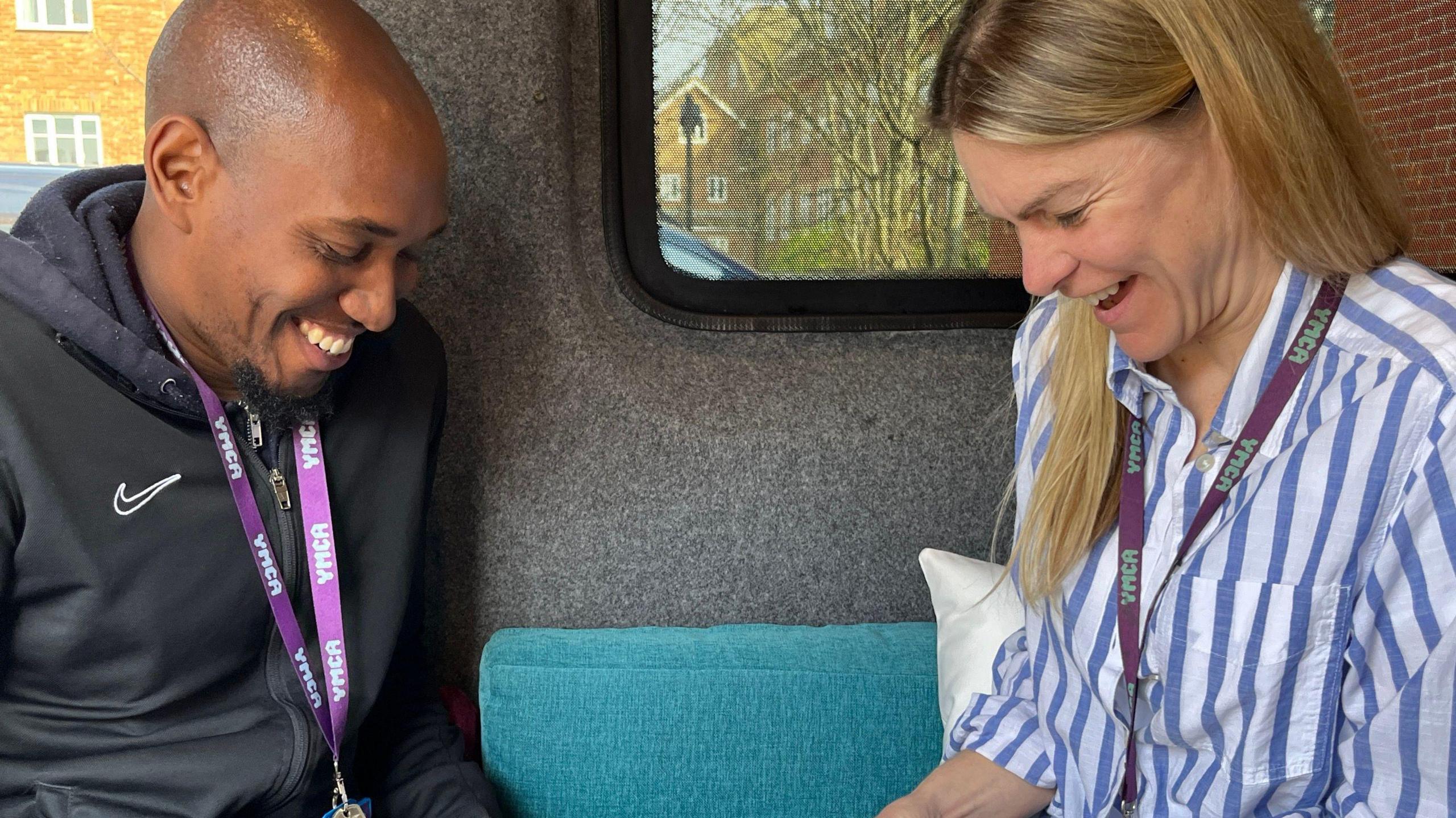 Marlon Williams (left, a man in a black tracksuit with a purple lanyard) and Fiona Oldam (right, a woman in a blue and white striped top with a purple lanyard) both smiling and looking down 