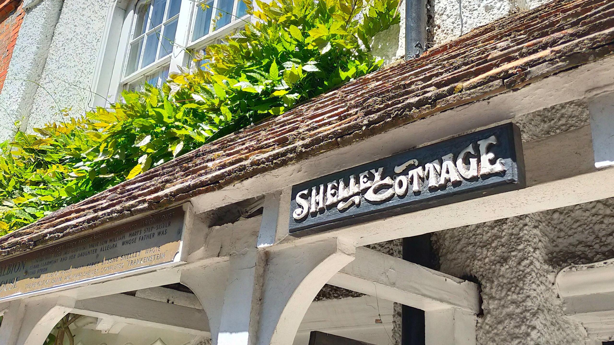The front of a residential house with the sign "Shelley Cottage" displayed outside and a bronze plaque nearby.