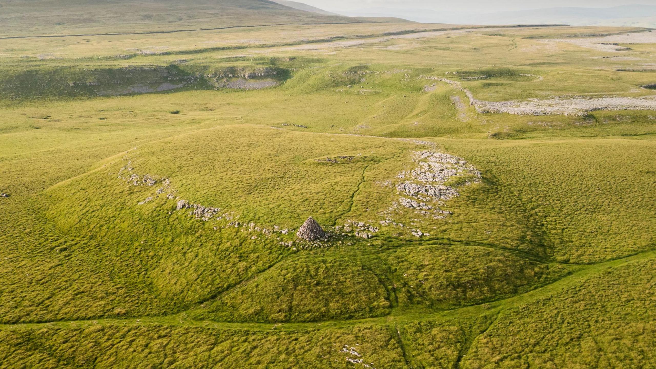 General view with Yorkshire Dales National Park surrounding the stone monument. The monument is in the centre of the image - the prominent conical cairn structure nearer the bottom is more modern and not part of the scheduling.