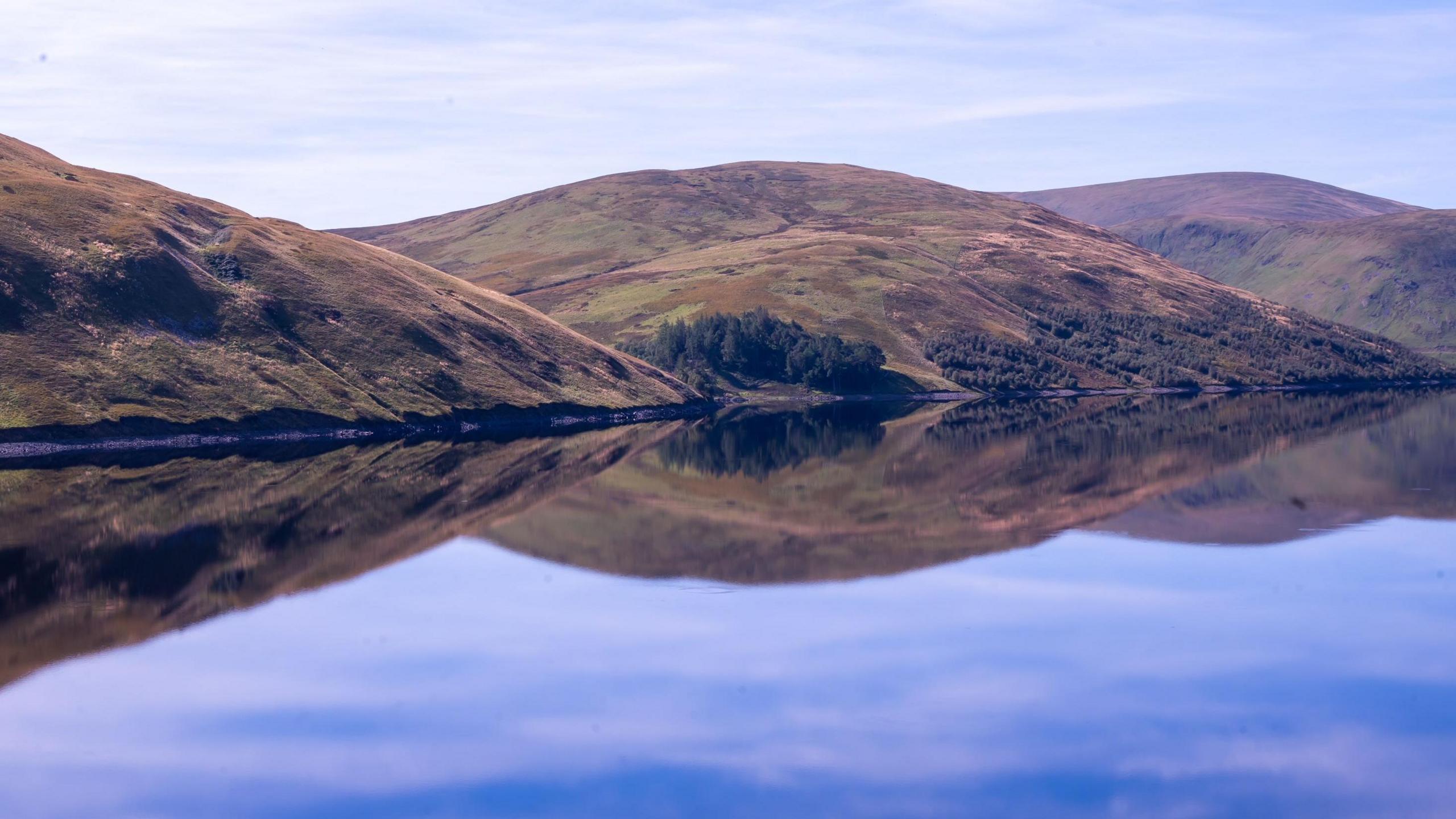 A set of hills reflected perfectly in the still waters of a reservoir.