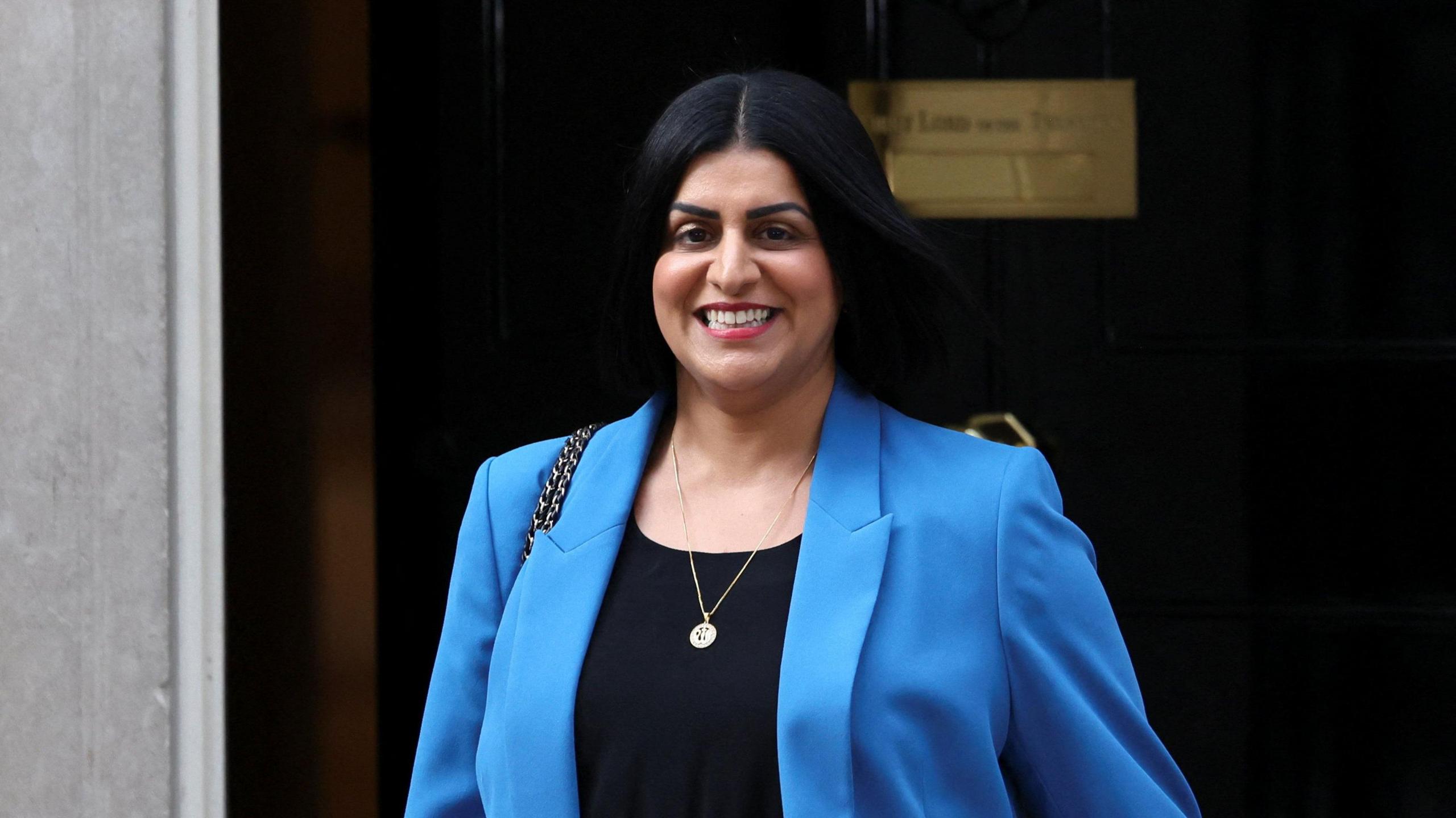 Shabana Mahmood, walking down Downing Street, smiling and wearing a blue blazer.
