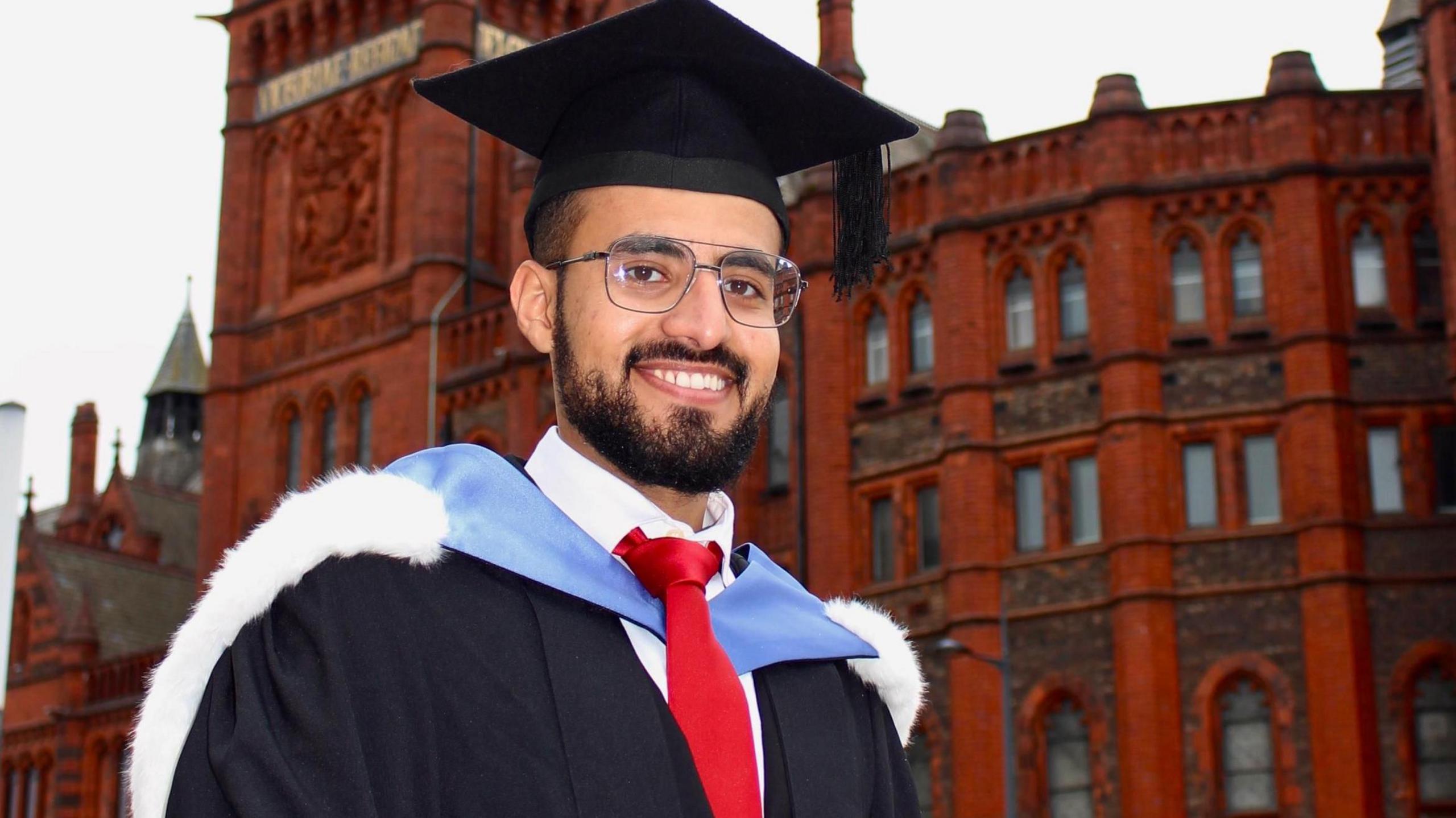 Hamza Al-Huseini when he was graduating from the University of Liverpool in 2020. He is standing in his cap and gown outside the red-brick Victoria Building.