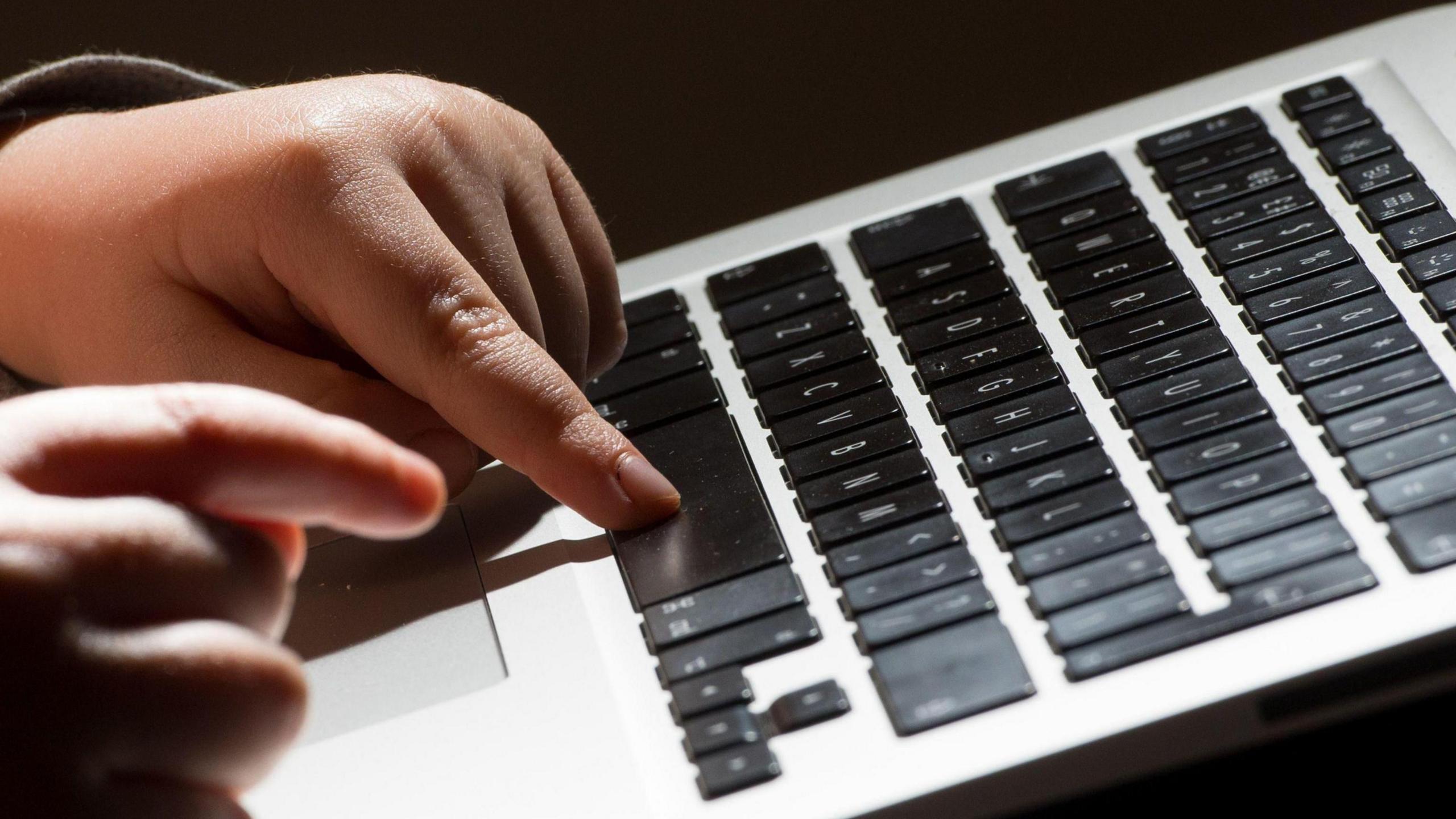 Fingers pressing the space bar on a laptop, with the keyboard seen tilted upwards. The keys are black with white letters
