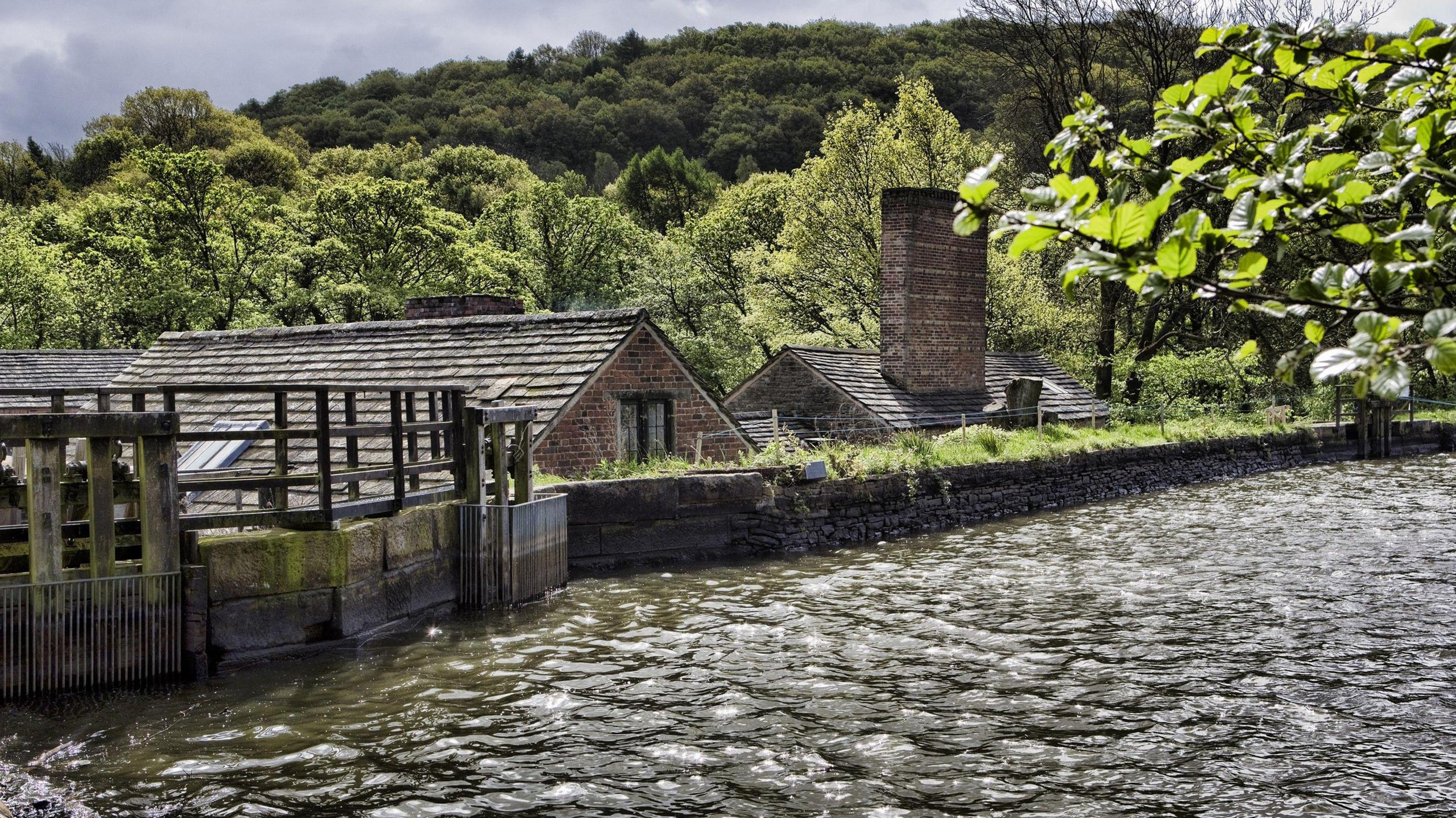 A dam with a stone wall in the foreground. Roofs of stone buildings can be seen beyond the wall.