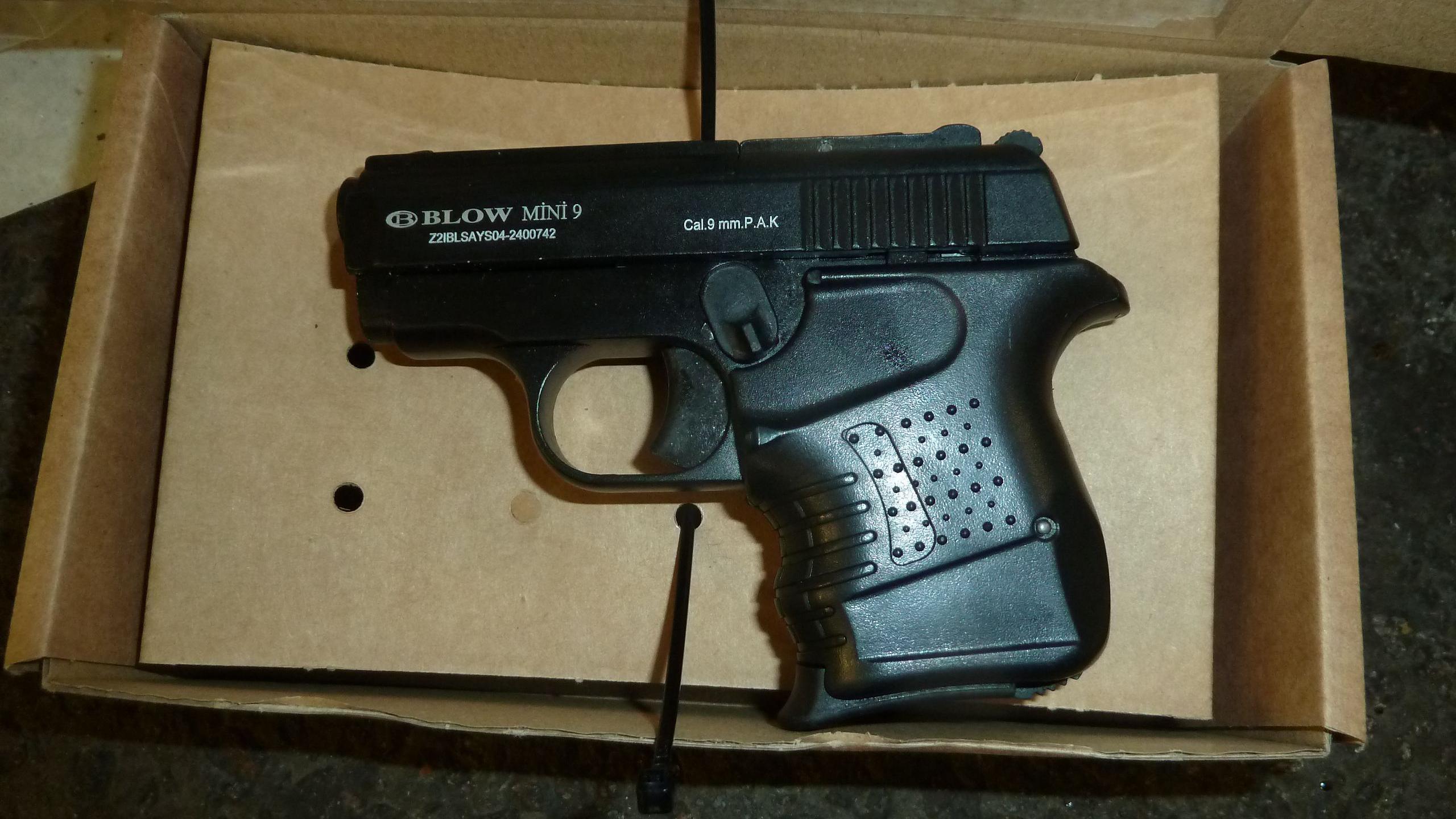 A small, chunky black gun in a box. It has small white writing on the gun.