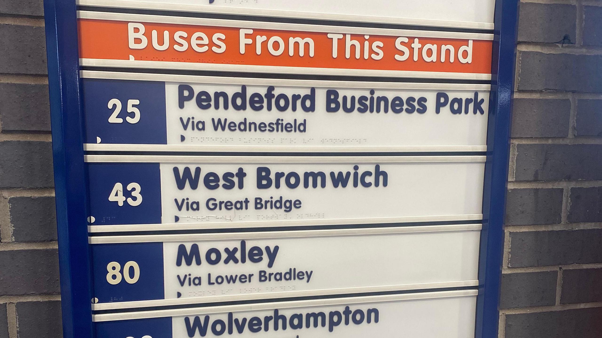 Picture showing bus services listed on a sign, including the number 80 to Moxley. It is written in blue with a white background. There are grey bricks behind the sign.