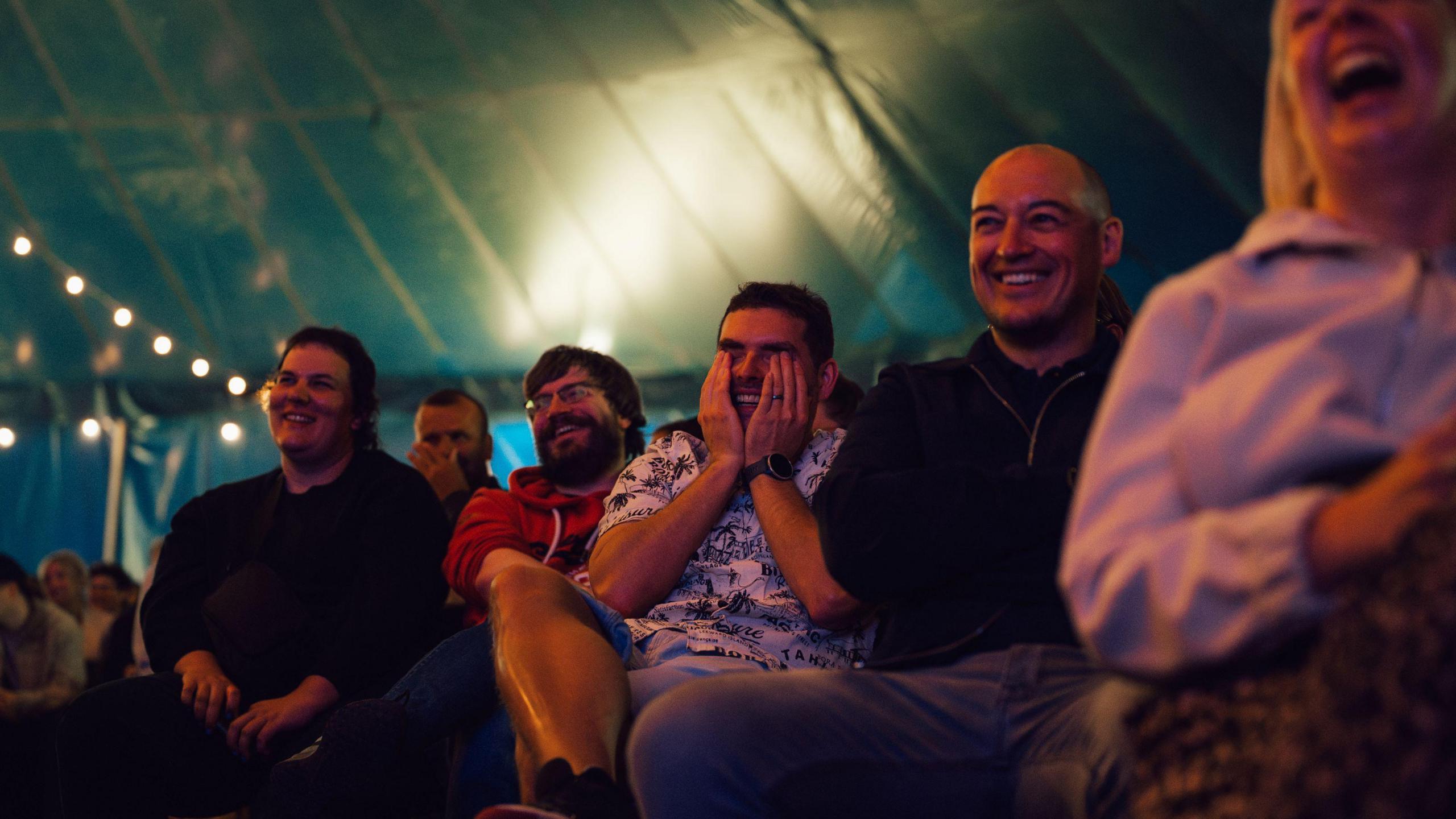 A group of people sitting and laughing together at a gig as part of the Bristol Comedy Garden.