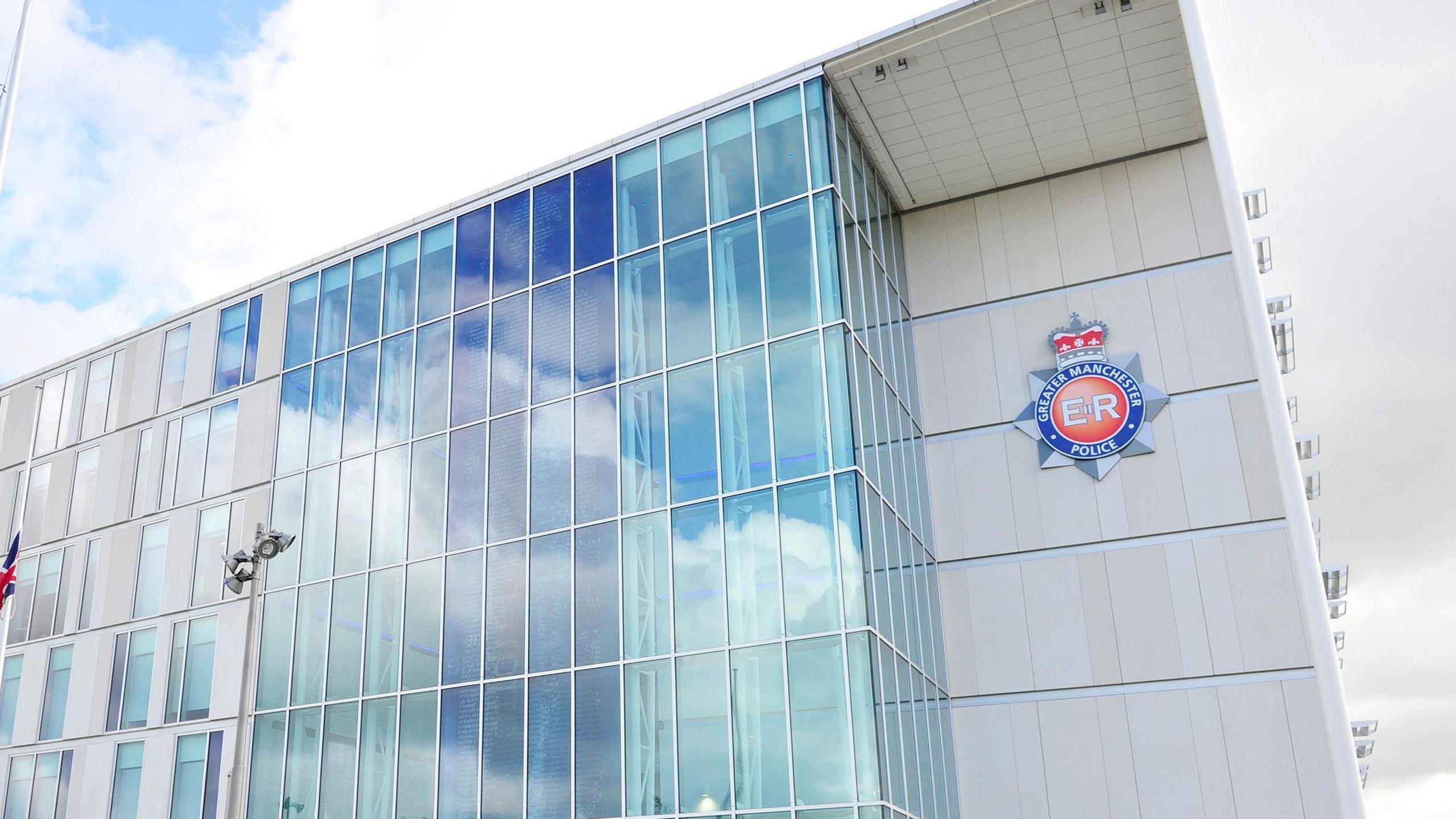 The glass-panelled front of the Greater Manchester Police headquarters building, which includes the force's blue and red police logo.