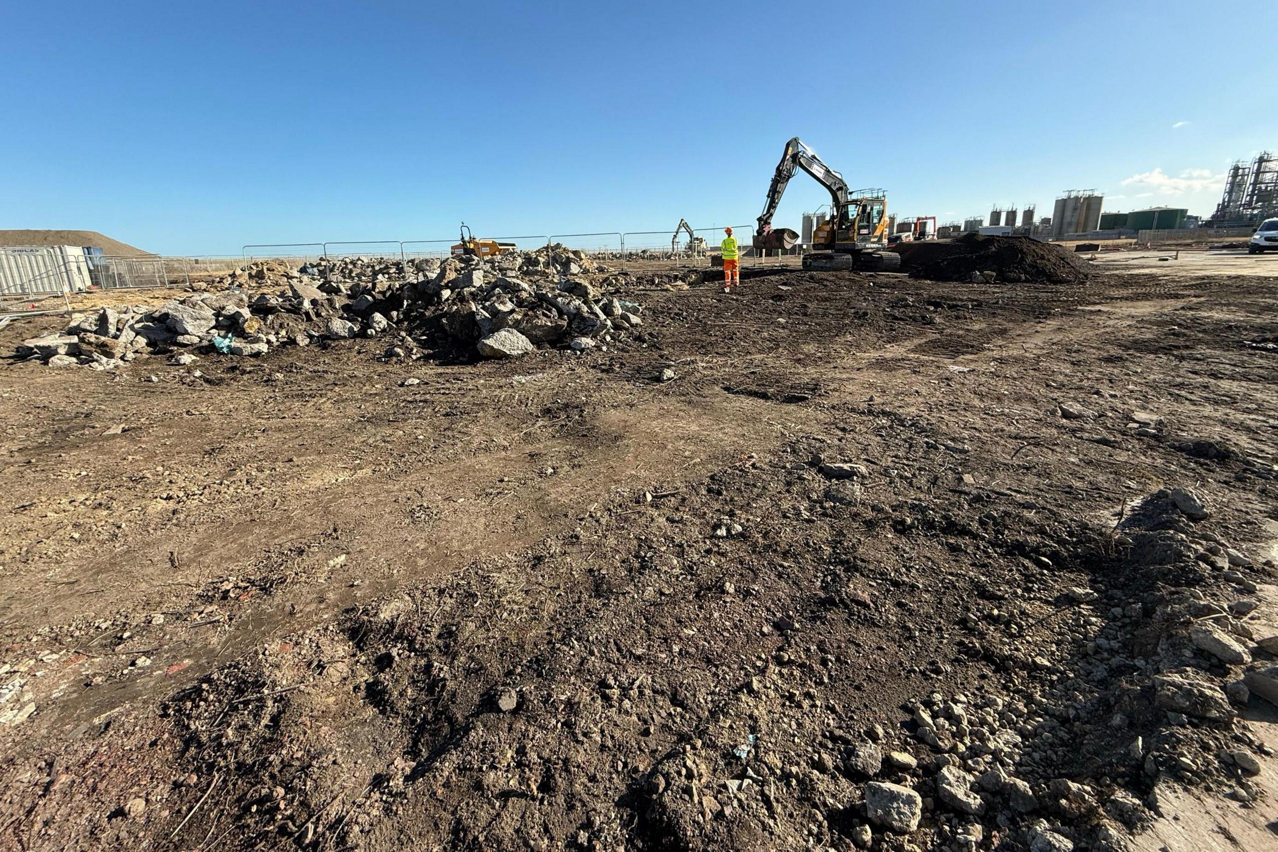 A mechanical digger and a worker stand at the Wastefront site, which is currently all dirt.