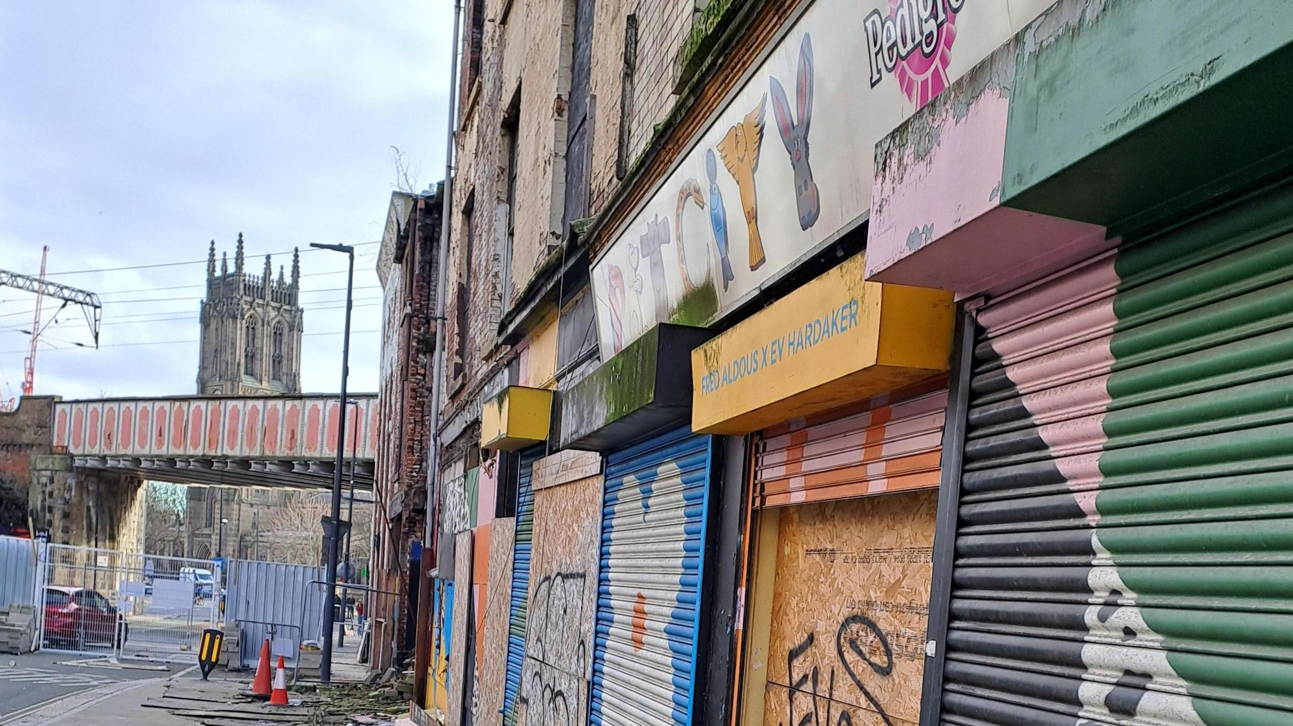 A closed street with a series of abandoned boarded up buildings on the left hand side of the road