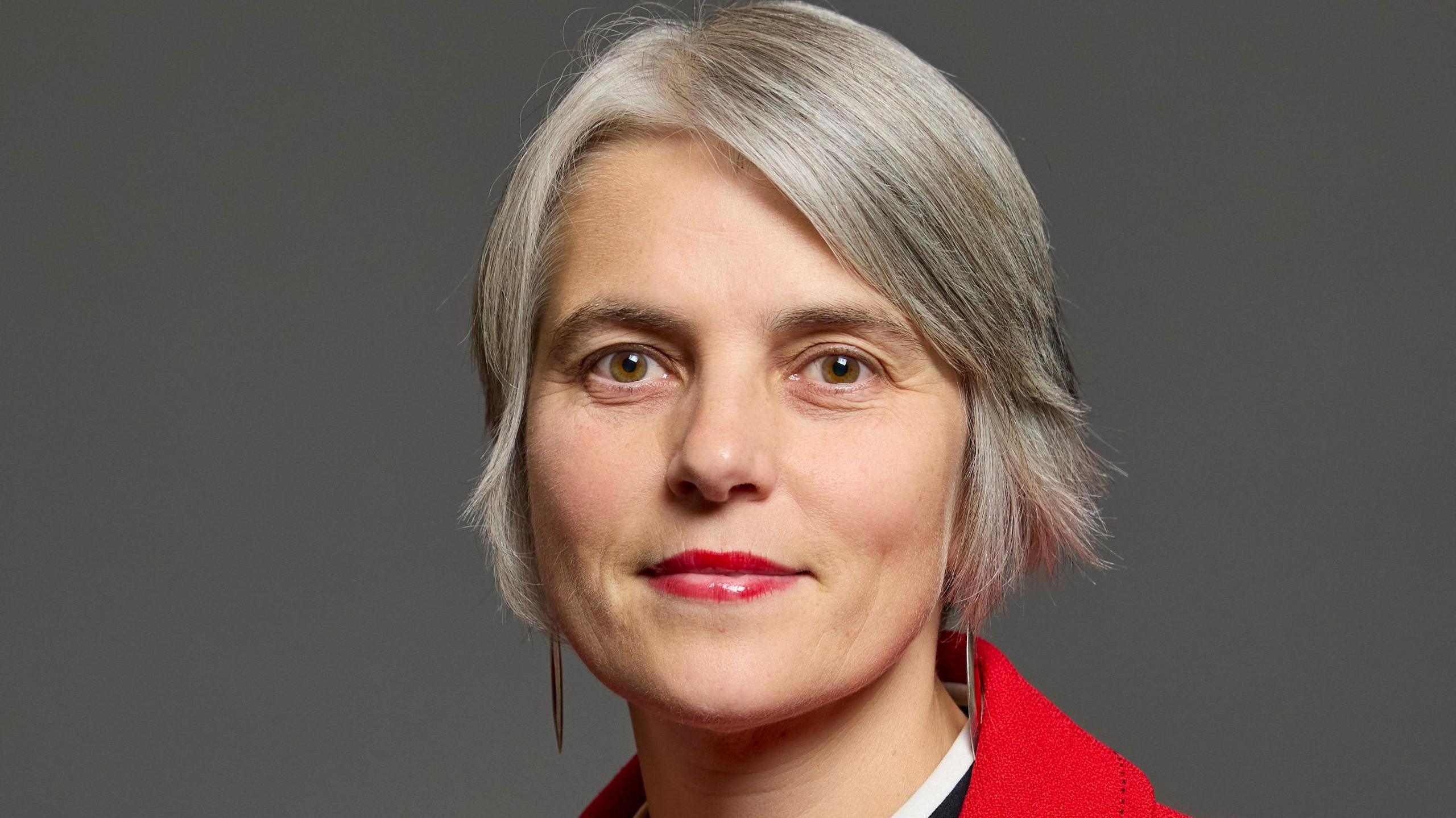 Anna Dixon: a woman with short grey hair wearing a red coat and red lipstick