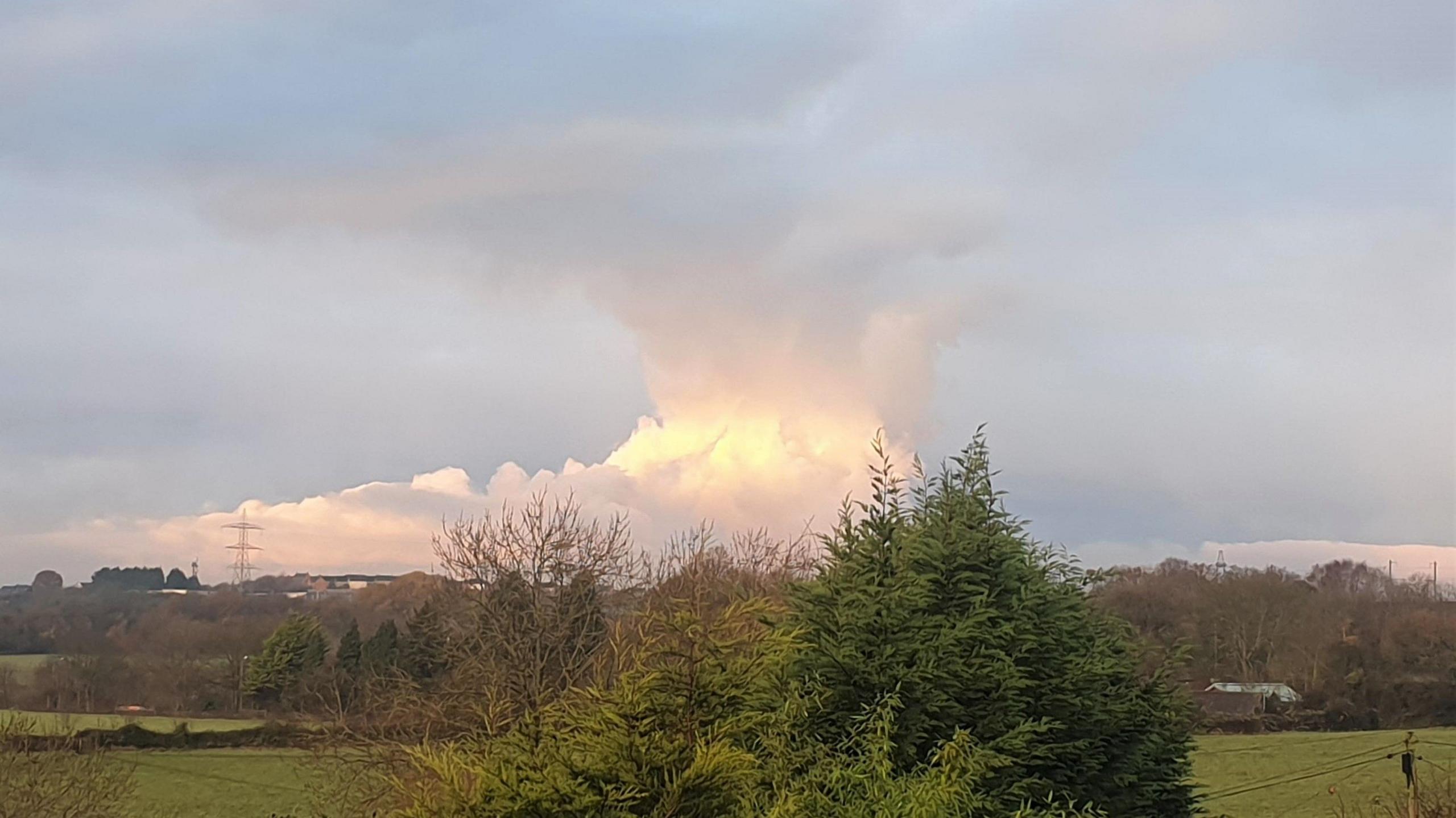 A towering mass of cloud rises behind the distant landscape, looking very much like a threatening thunderstorm.