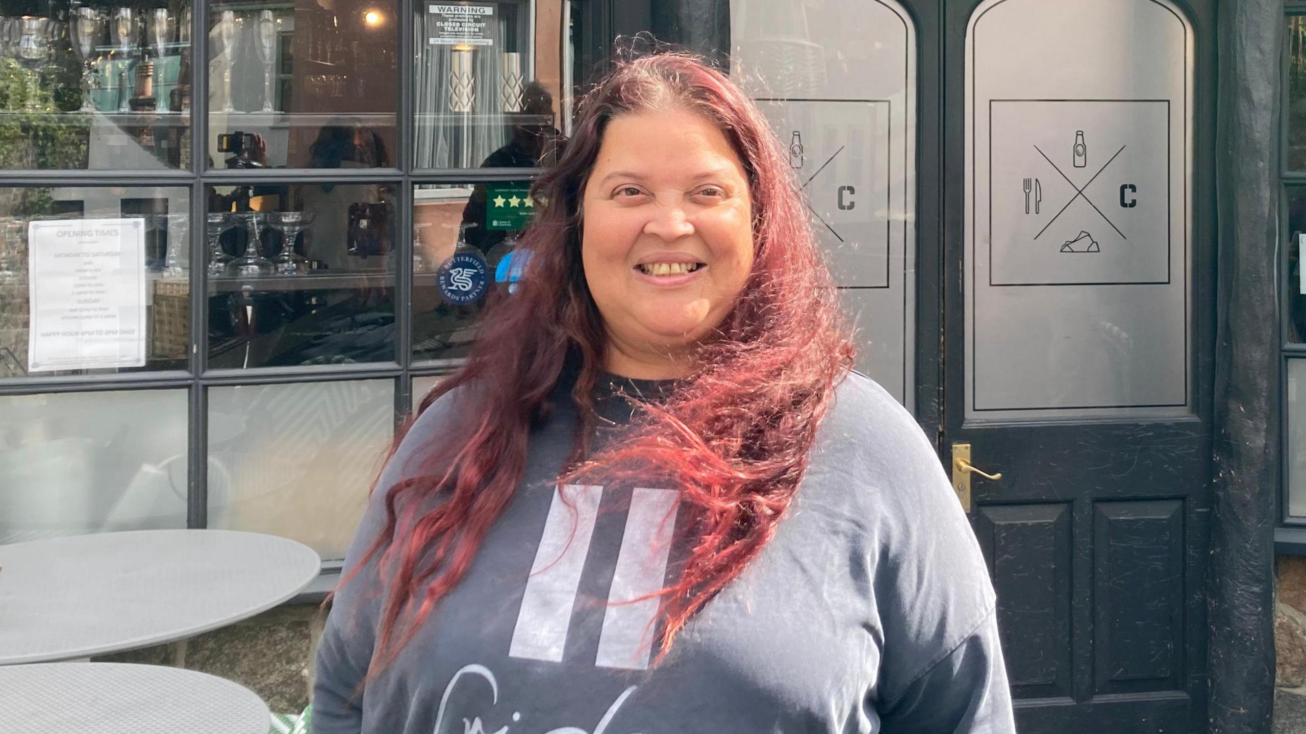 A woman with long red hair smiling outside of a black building with gold lettering that says the Cornerstone.