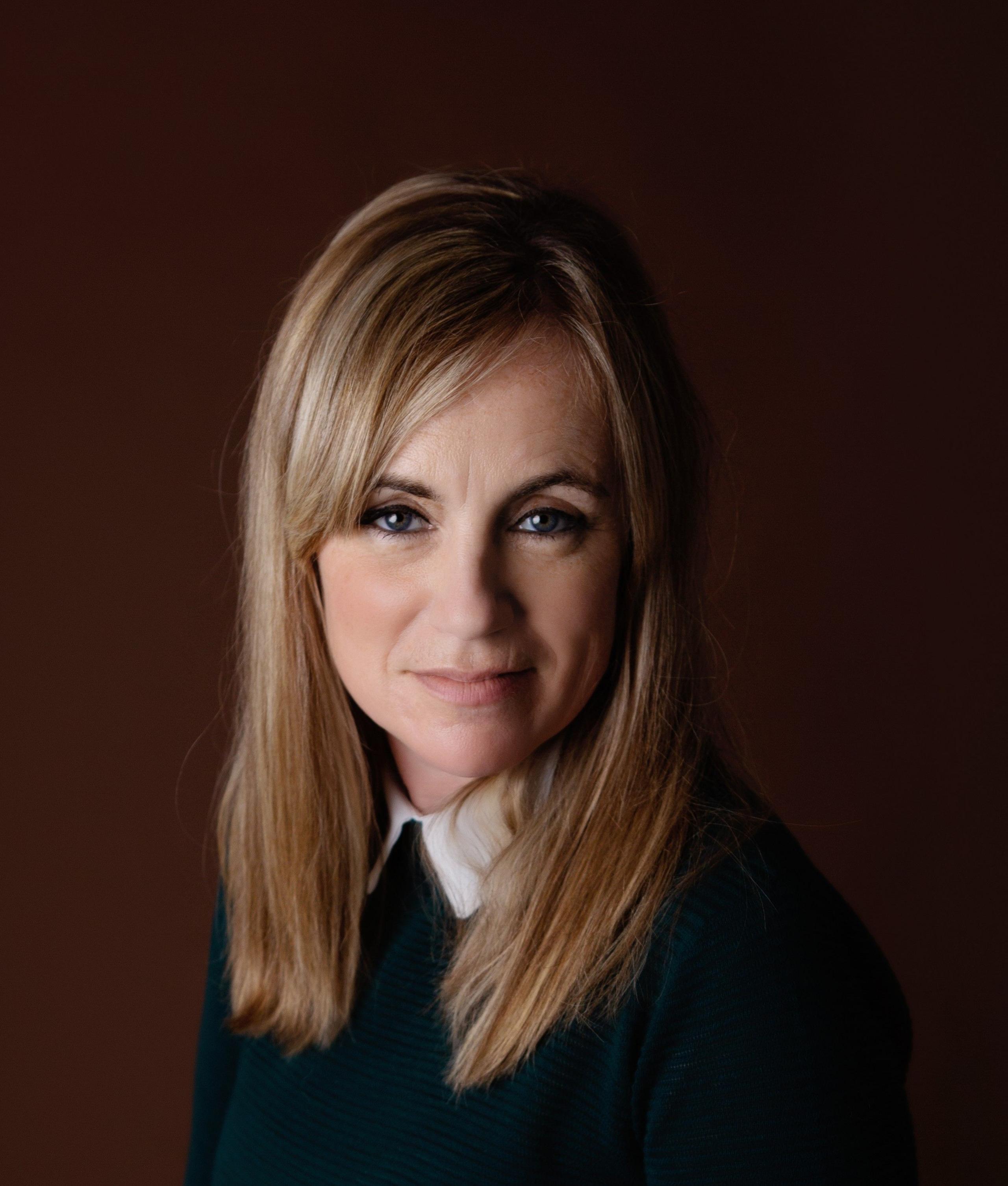 Dr Helen Bichard has blonde hair, and faces the camera with a neutral expression. She is wearing a black top with a white collar. 