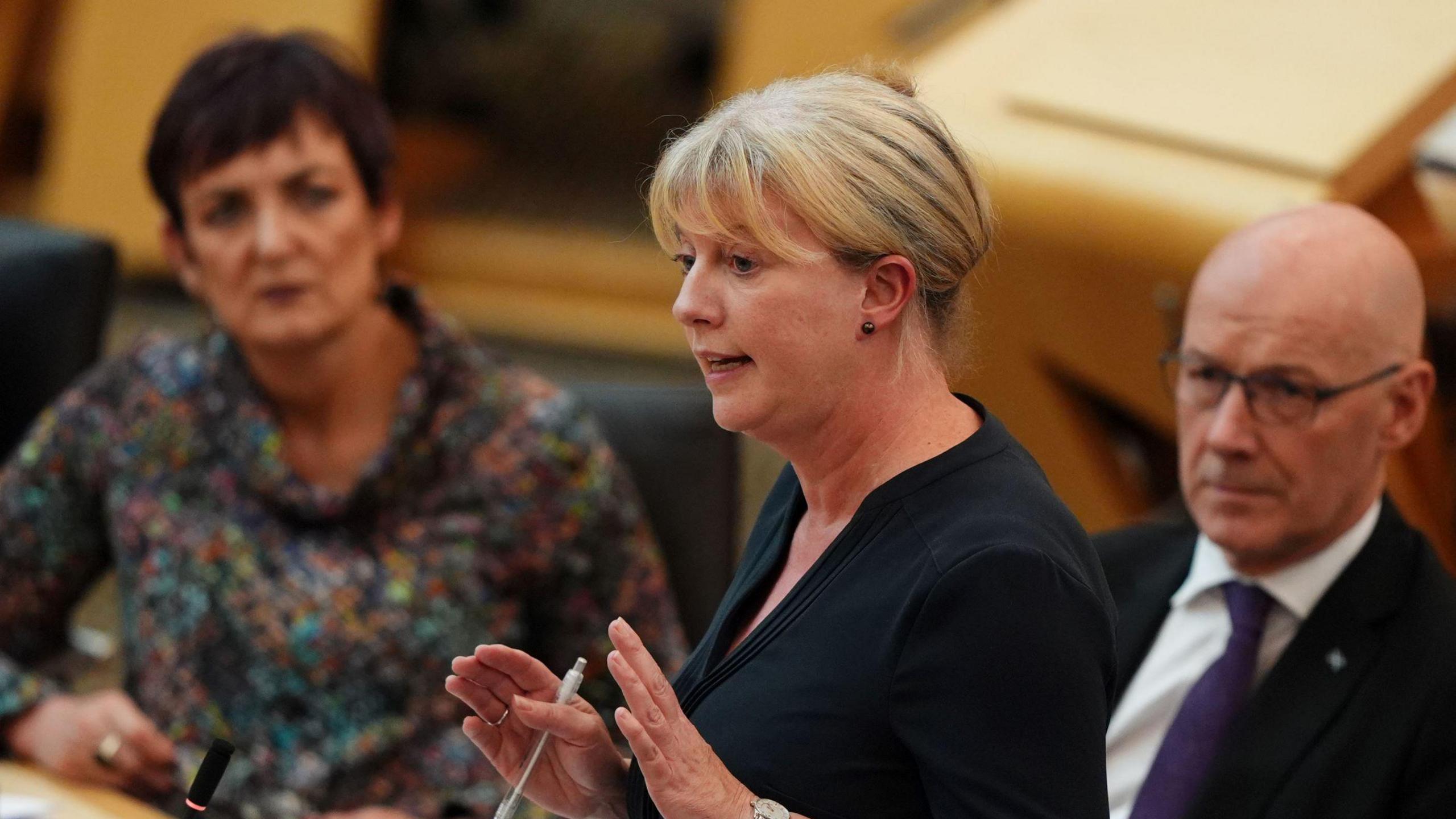 Shona Robison speaking in the Scottish Parliament, watched by the first minister John Swinney.  