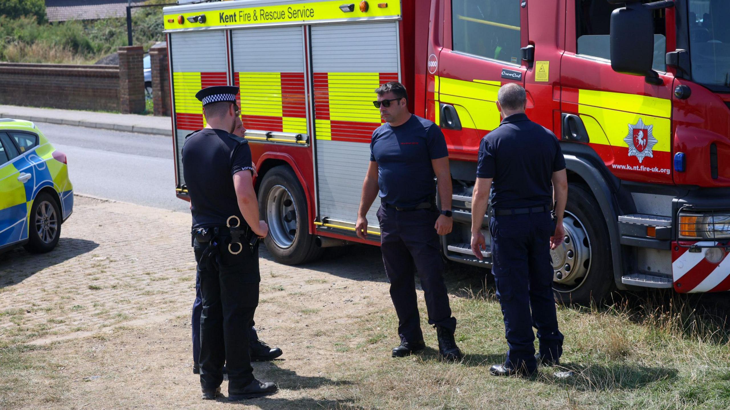 Police officers and fire crews stand in front of a fire engine.