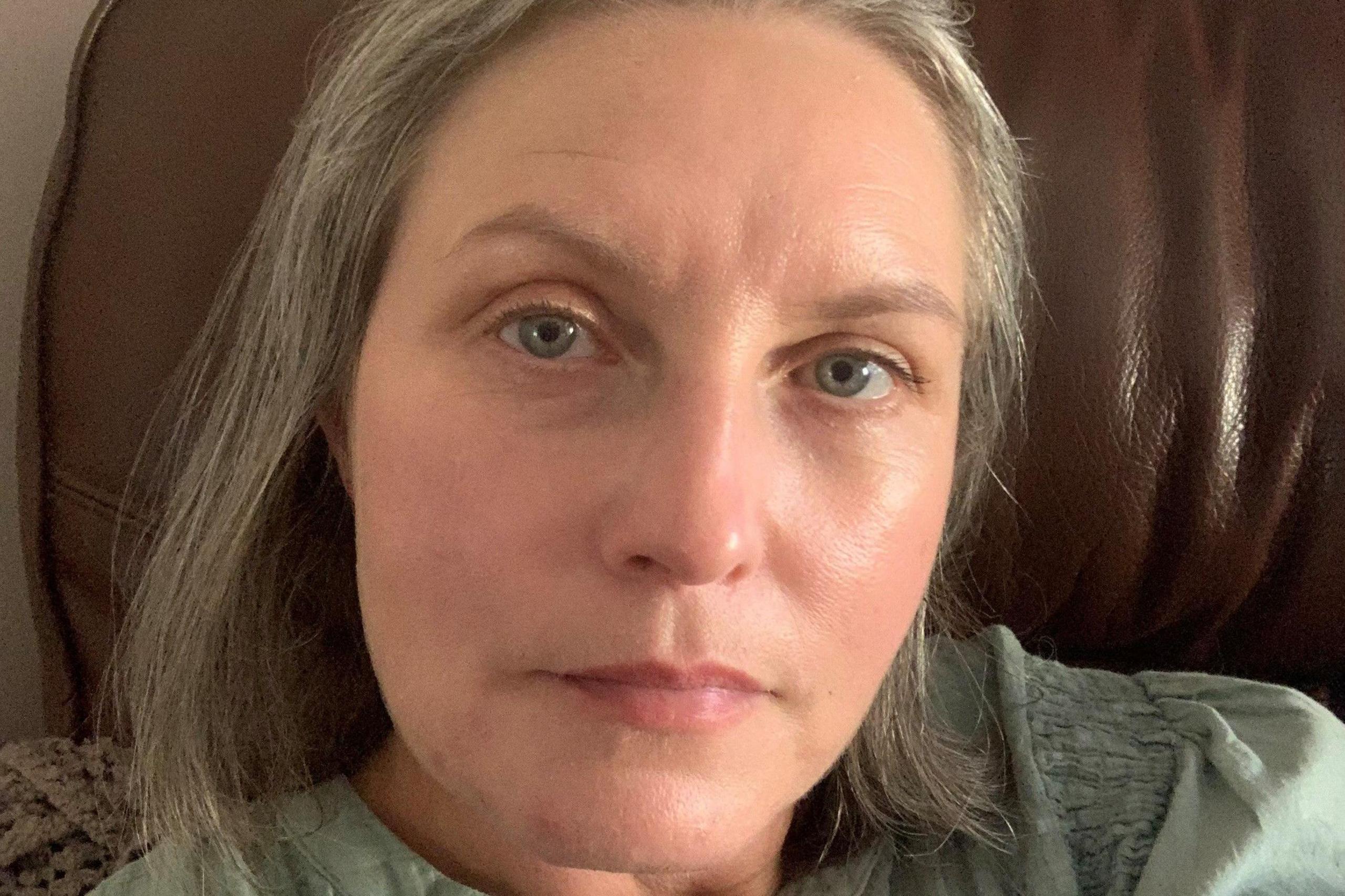 Clare Rees is looking at the camera in a close up photo in a green/grey top. She has shoulder length grey hair and blue eyes.
