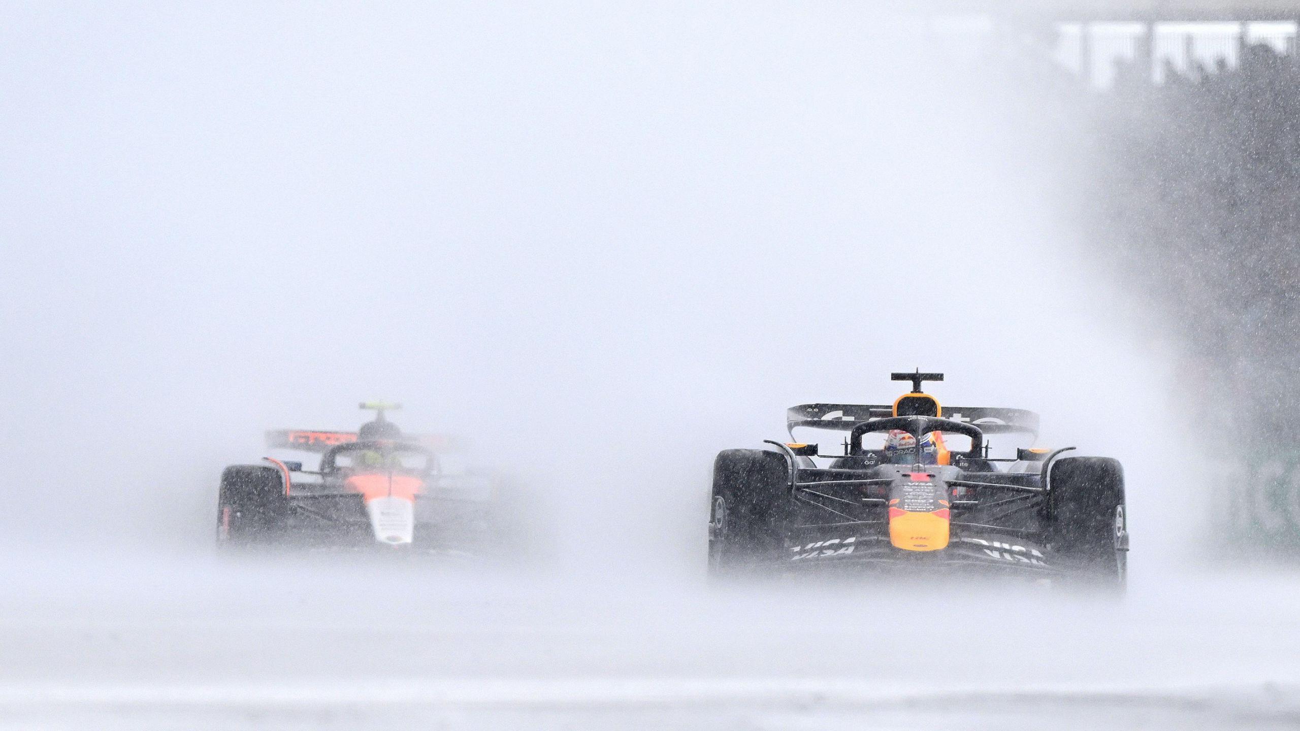 Red Bull's Max Verstappen with McLaren's Lando Norris in the background, with both cars throwing up spray during a torrential downpour during the 2025 British Grand Prix