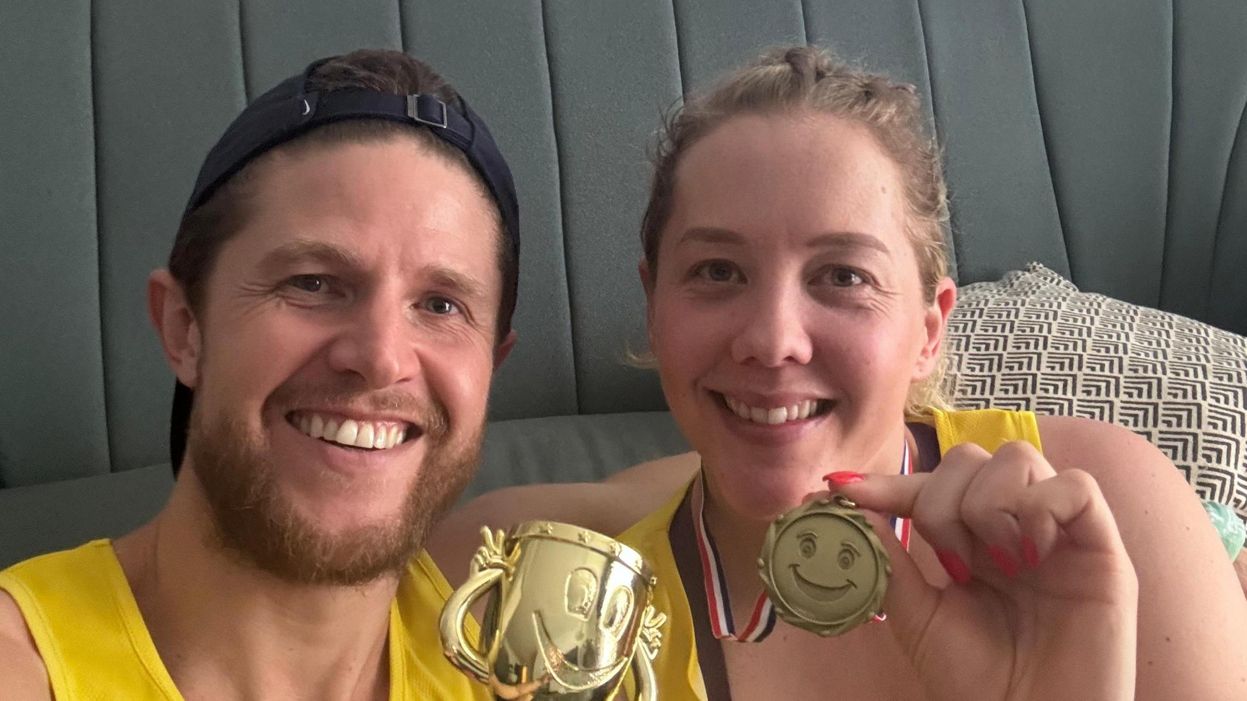 A man and woman smile holding medals and trophies