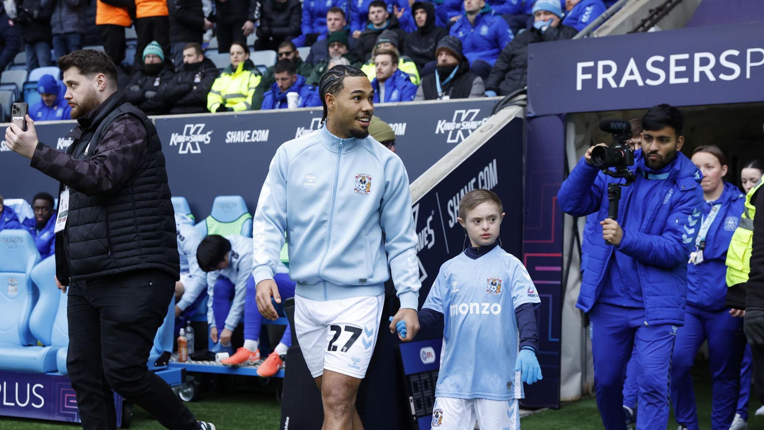 Milan van Ewijk wearing the Coventry City match day kit alongside Archie, who is wearing a Coventry City shirt, a blue undershirt and blue gloves