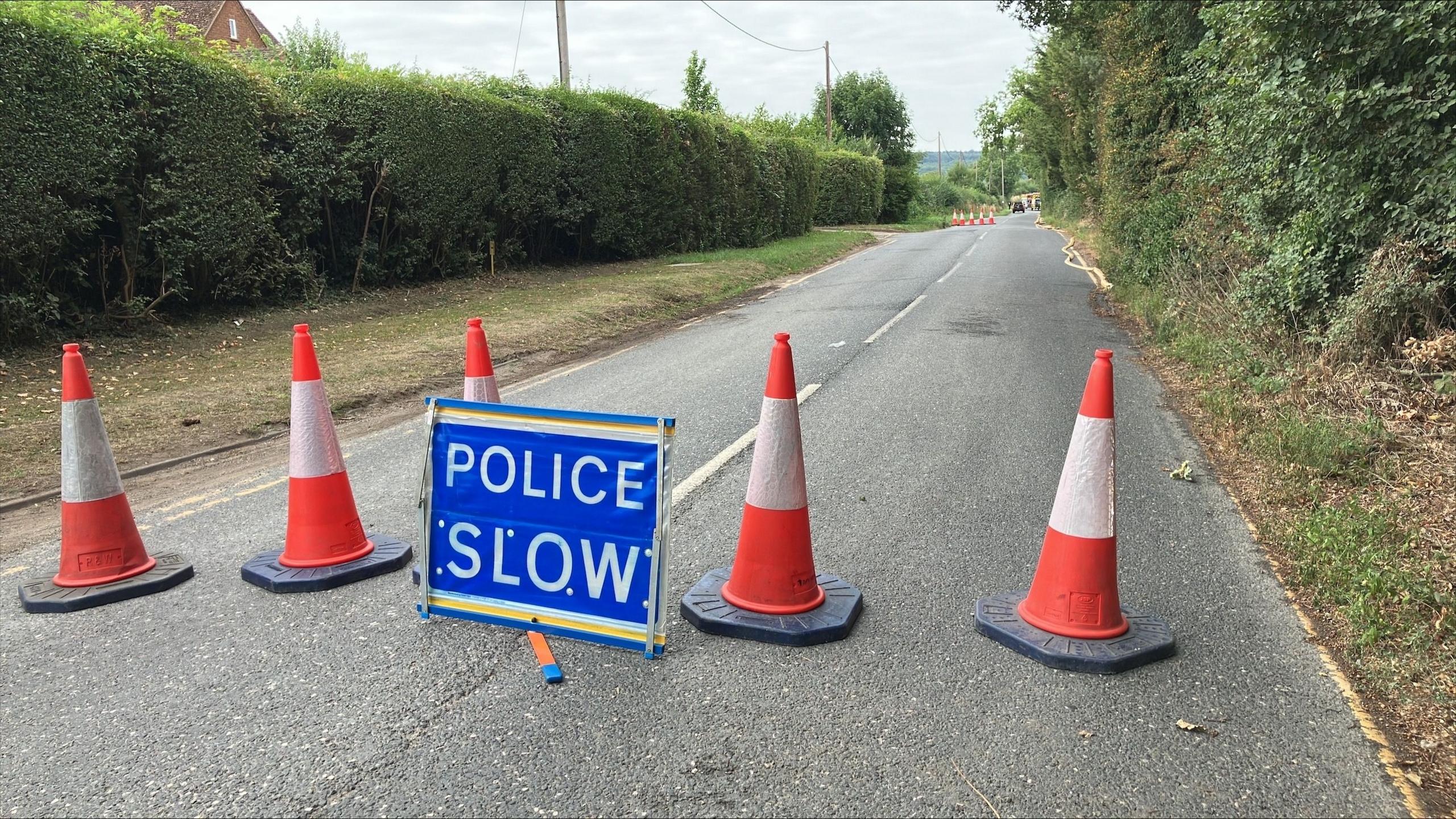 Orange and white cones with a 'police slow' sign on the road.