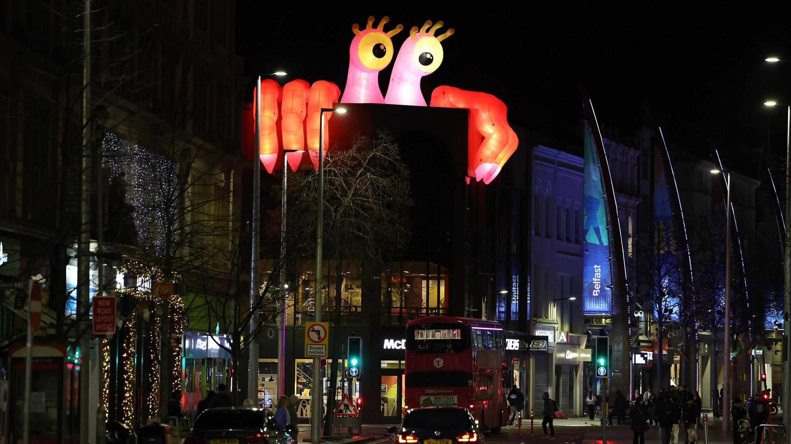 An inflatable monster peeking over the side of a building in Belfast city centre at night.