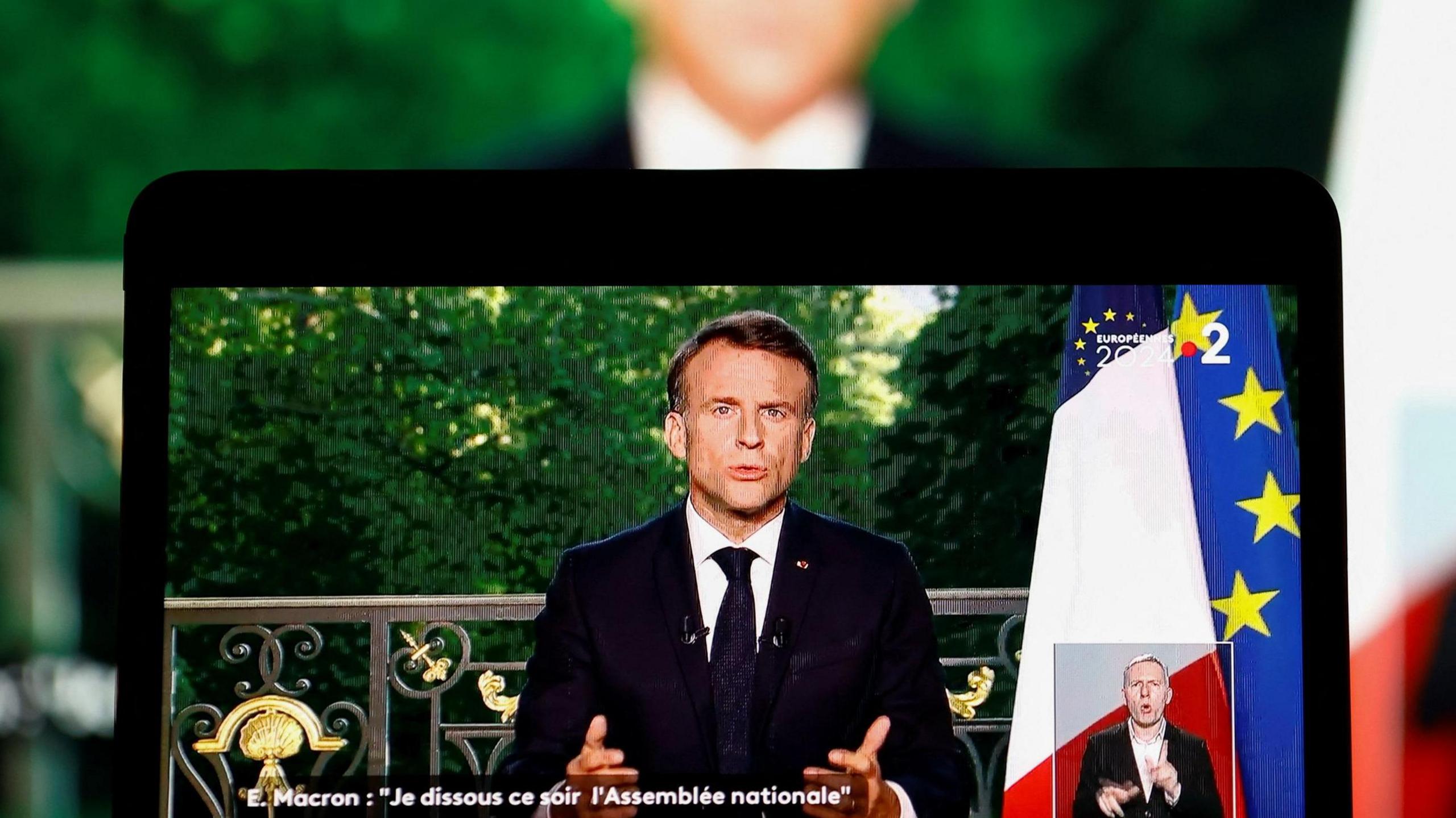 Emmanuel Macron giving his speech on a screen with him blurred behind too