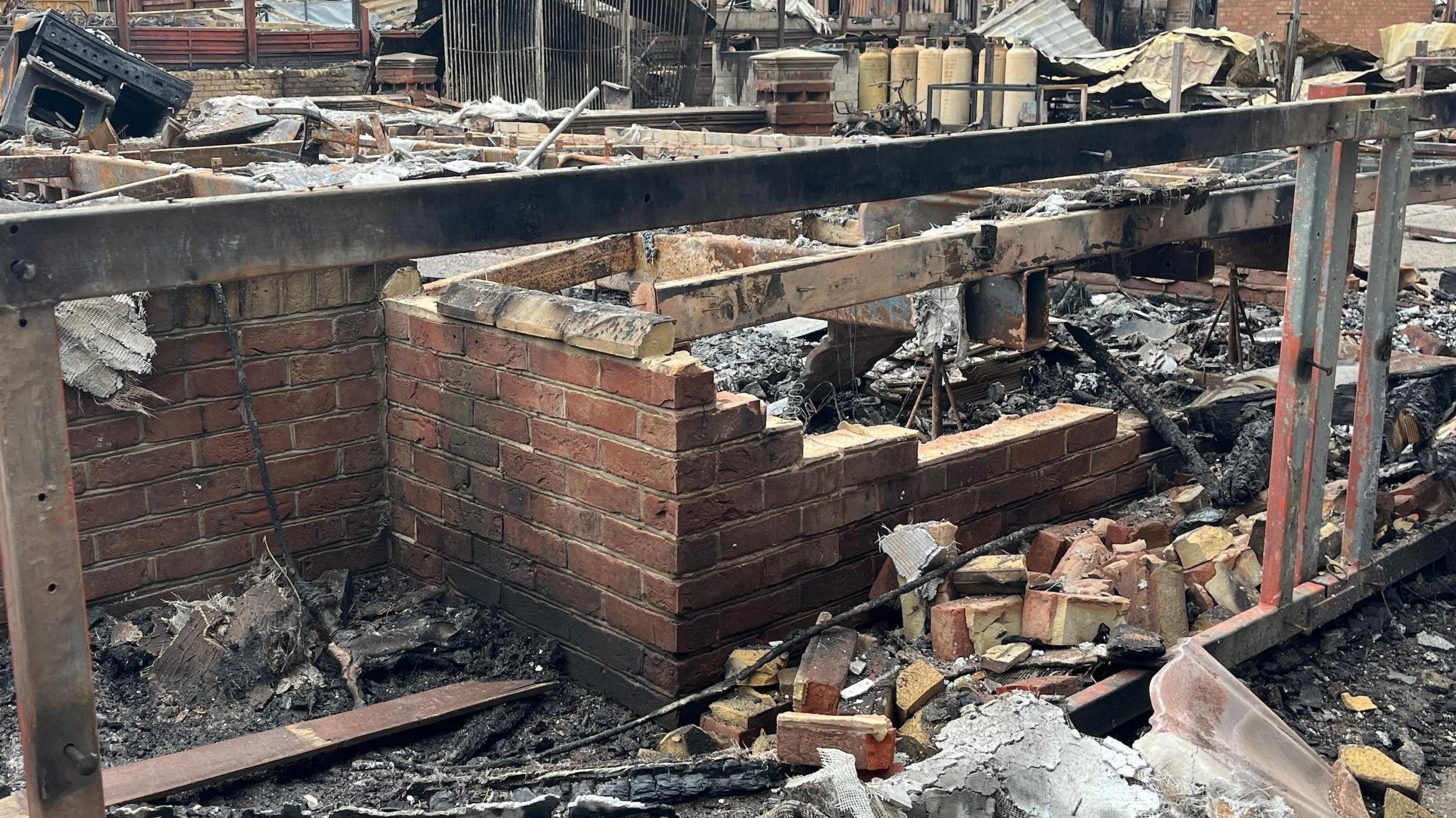 A burnt-down fence separating the charred and blackened remains of two caravans.