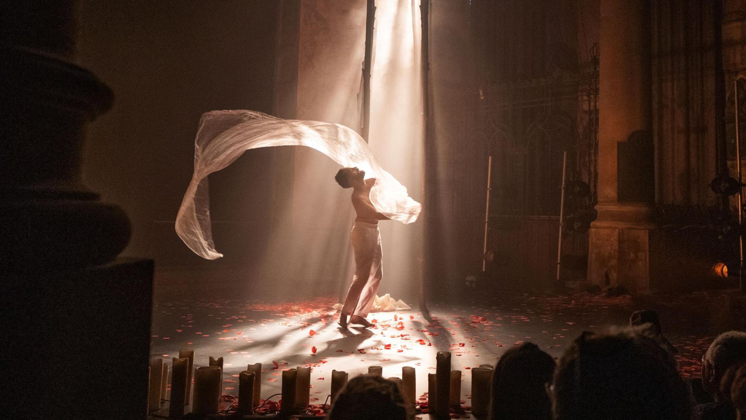 A performer called Aakash Odedra in a white outfit dances on stage during a show called Songs of the Bulbul