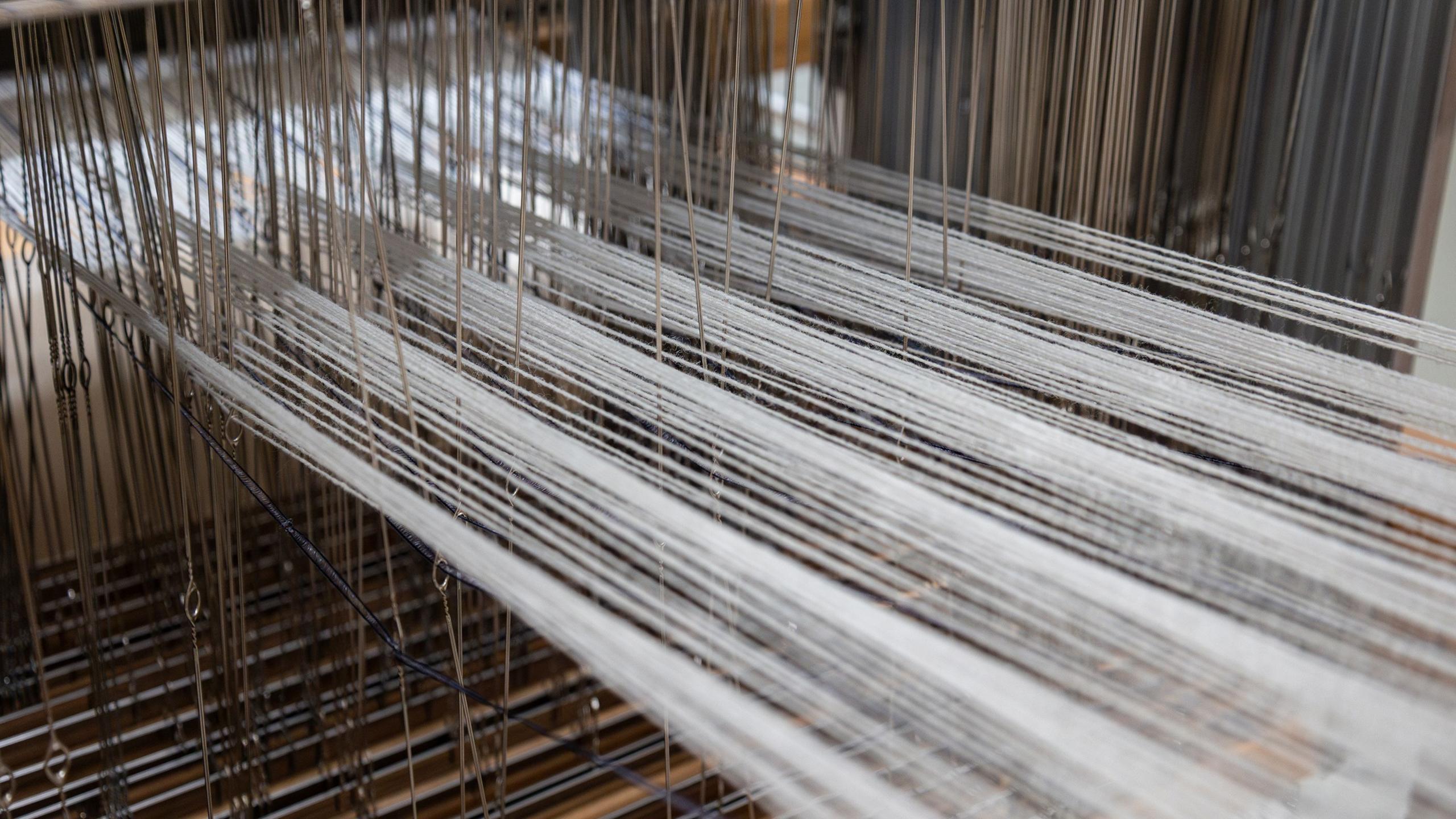 A close-up image of yarn being threaded through a loom