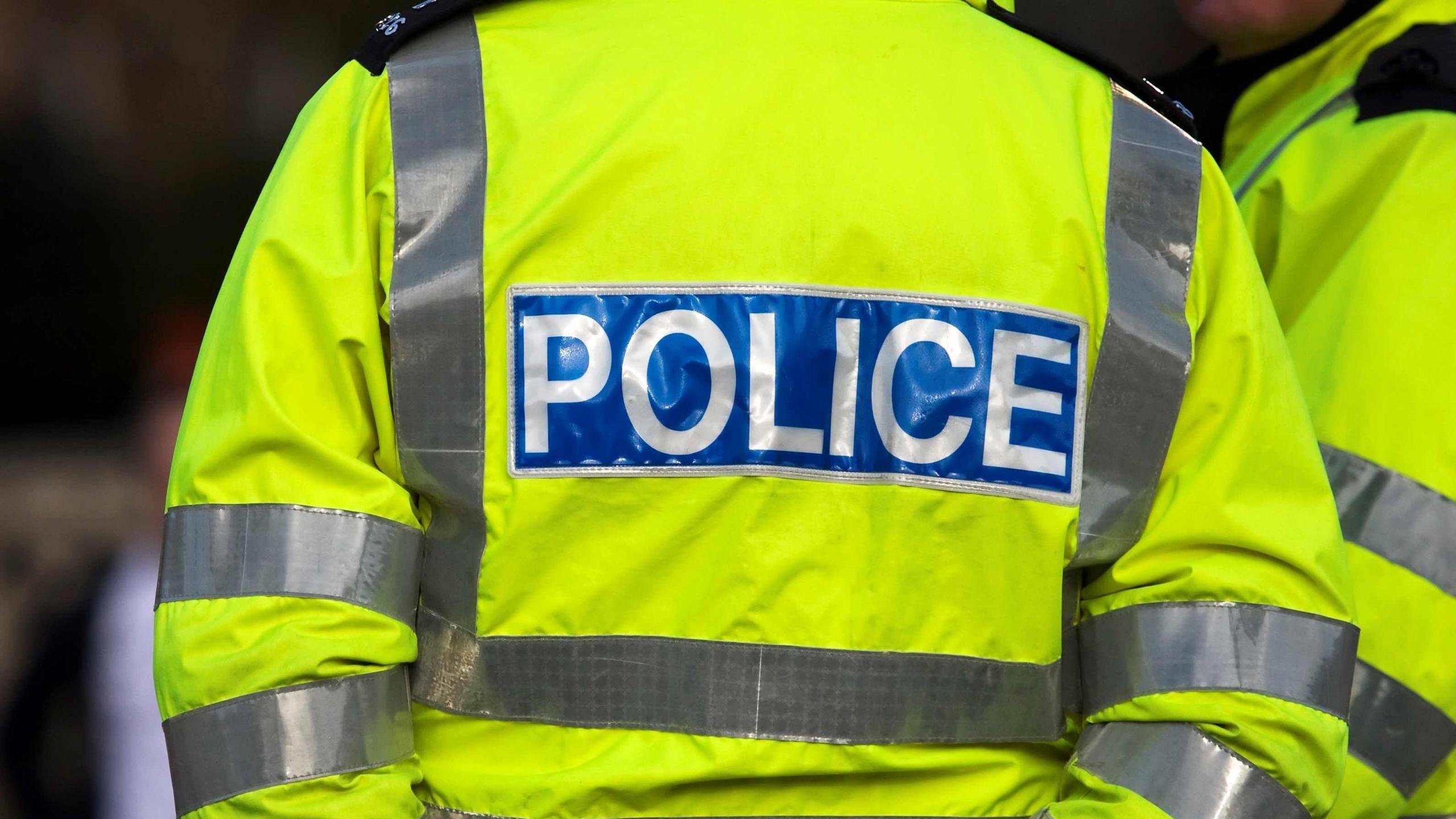 The back of a police officer, wearing a police jacket with Police written on it